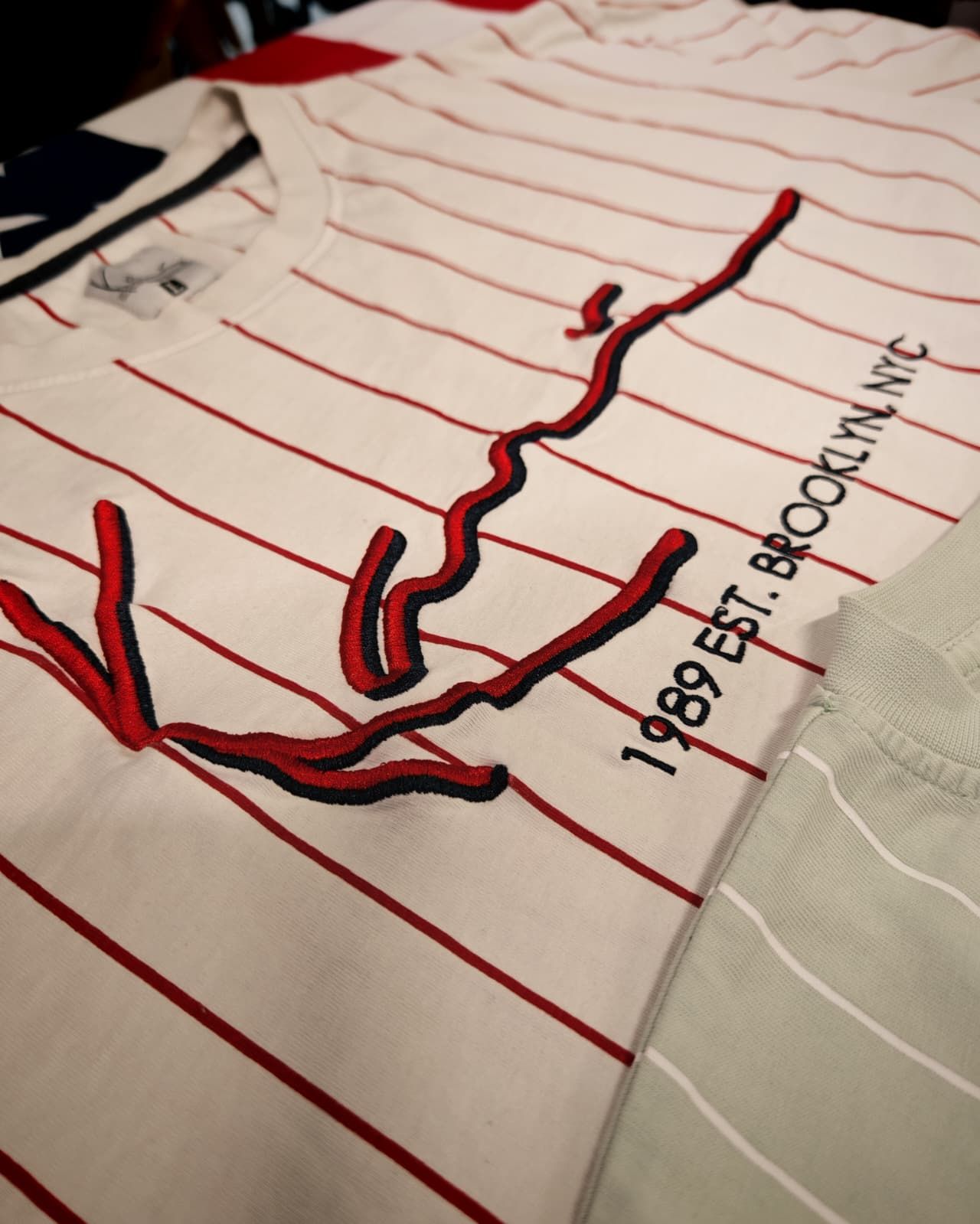 Primo piano di una camicia a righe bianche con un disegno di un albero ricamato in rosso e la scritta