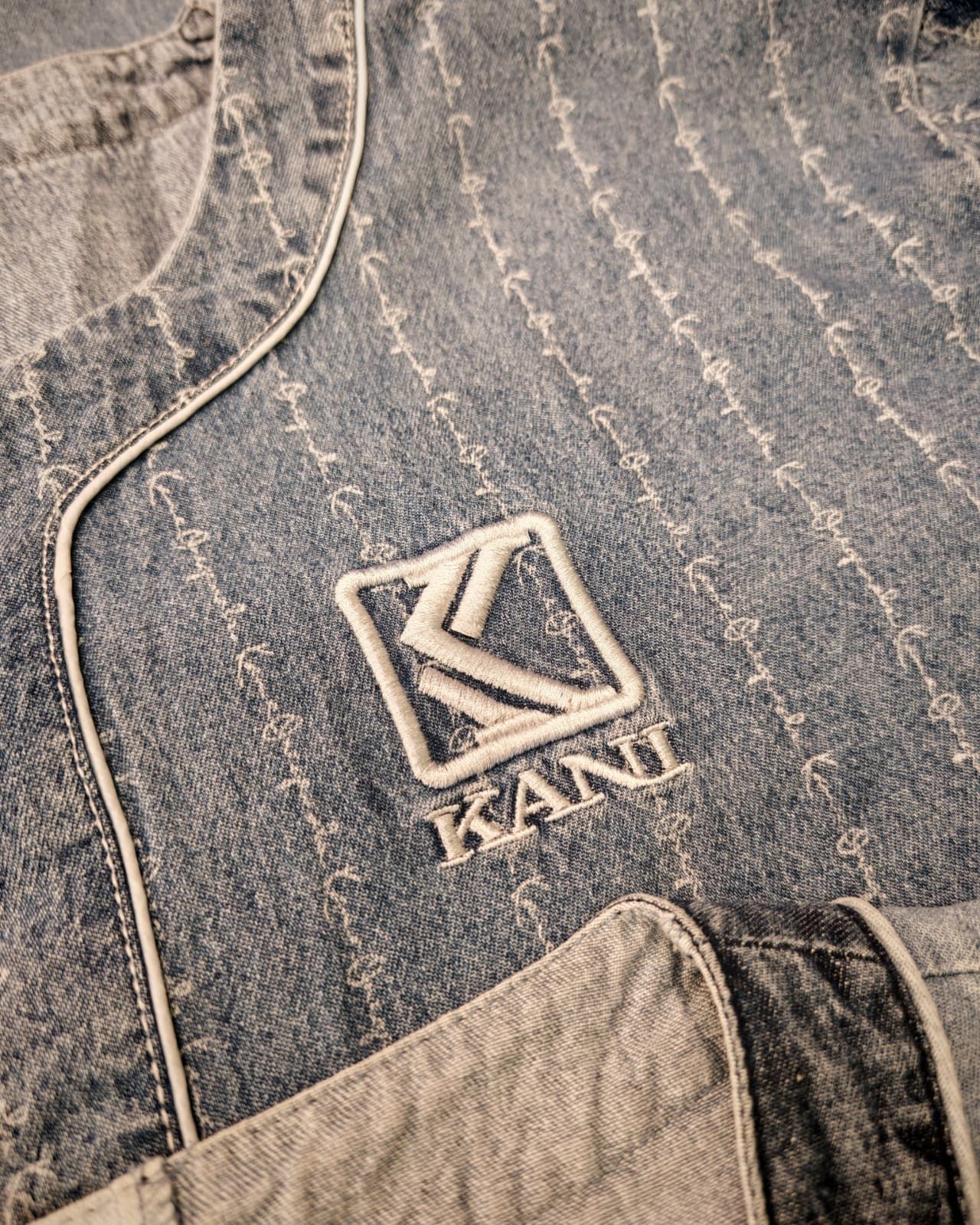 Primo piano di una giacca di jeans con logo K cucito e scritta KAMU sul petto.