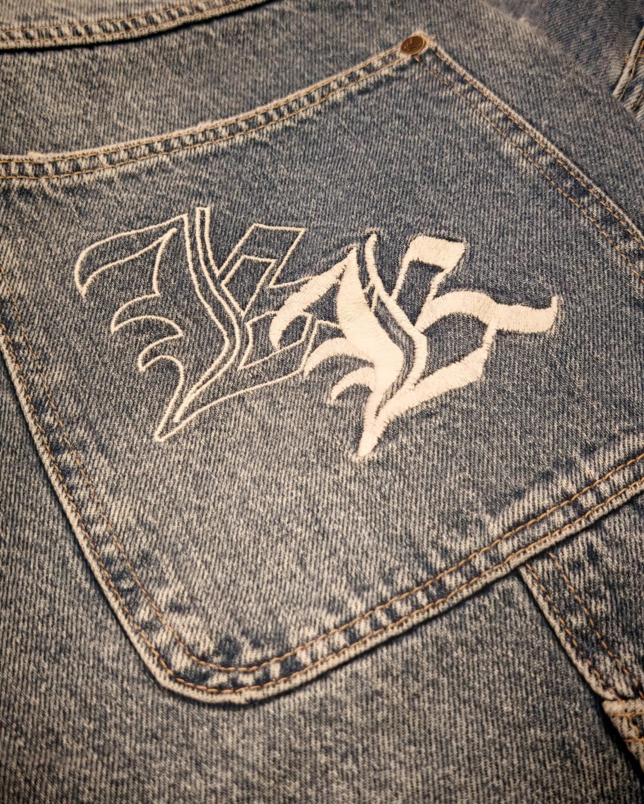 Primo piano di una tasca di una giacca di jeans con ricami bianchi in stile graffiti sul retro.