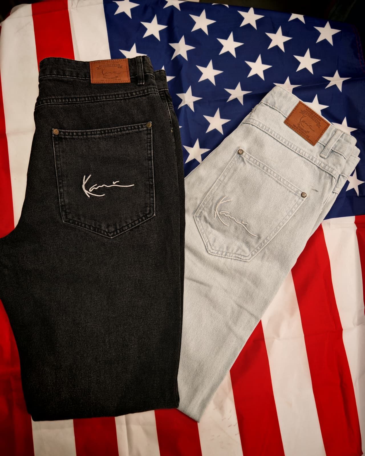 Due jeans piegati, uno nero e uno grigio chiaro, adagiati su uno sfondo con la bandiera americana.