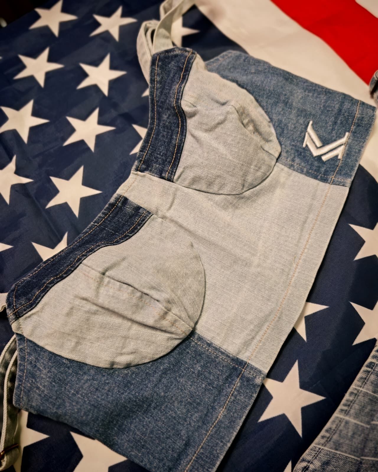 Indumento patchwork in denim con inserto grigio, adagiato su una coperta con la bandiera americana.