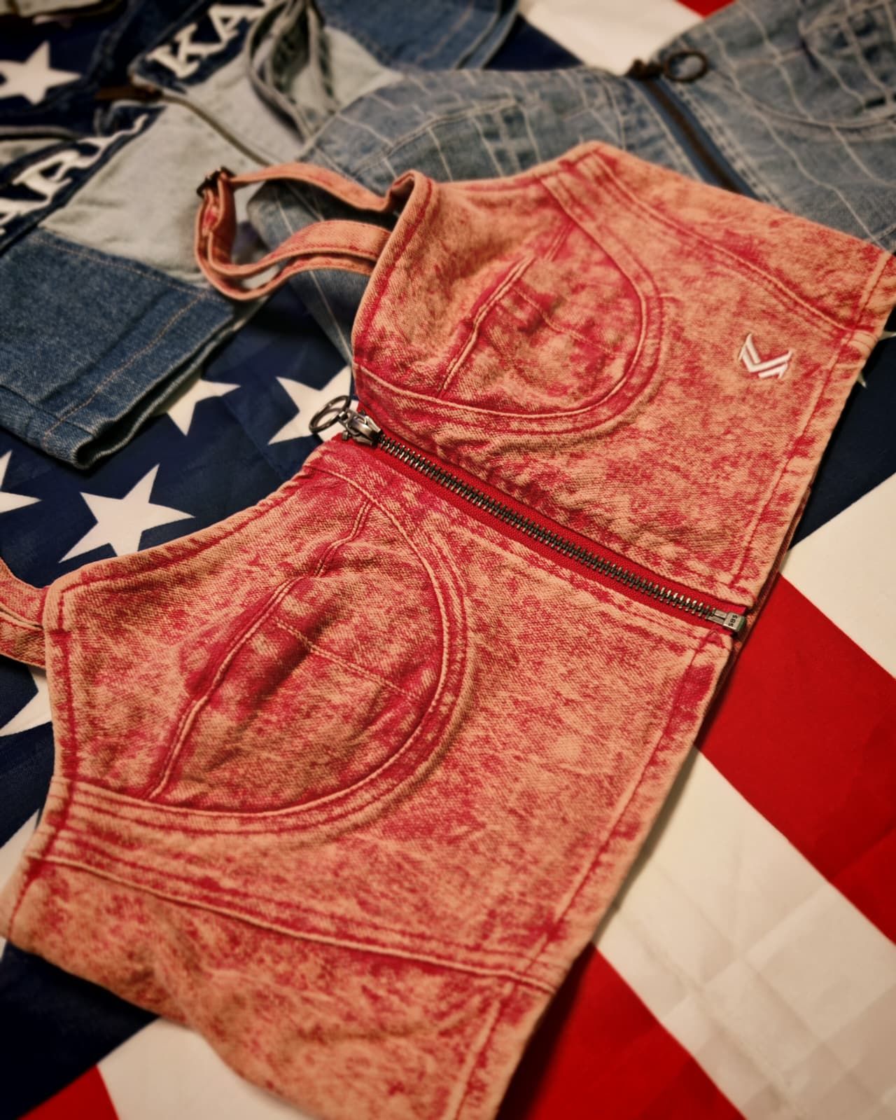 Top corto in denim rosso appoggiato su una bandiera americana, con dei jeans sullo sfondo.
