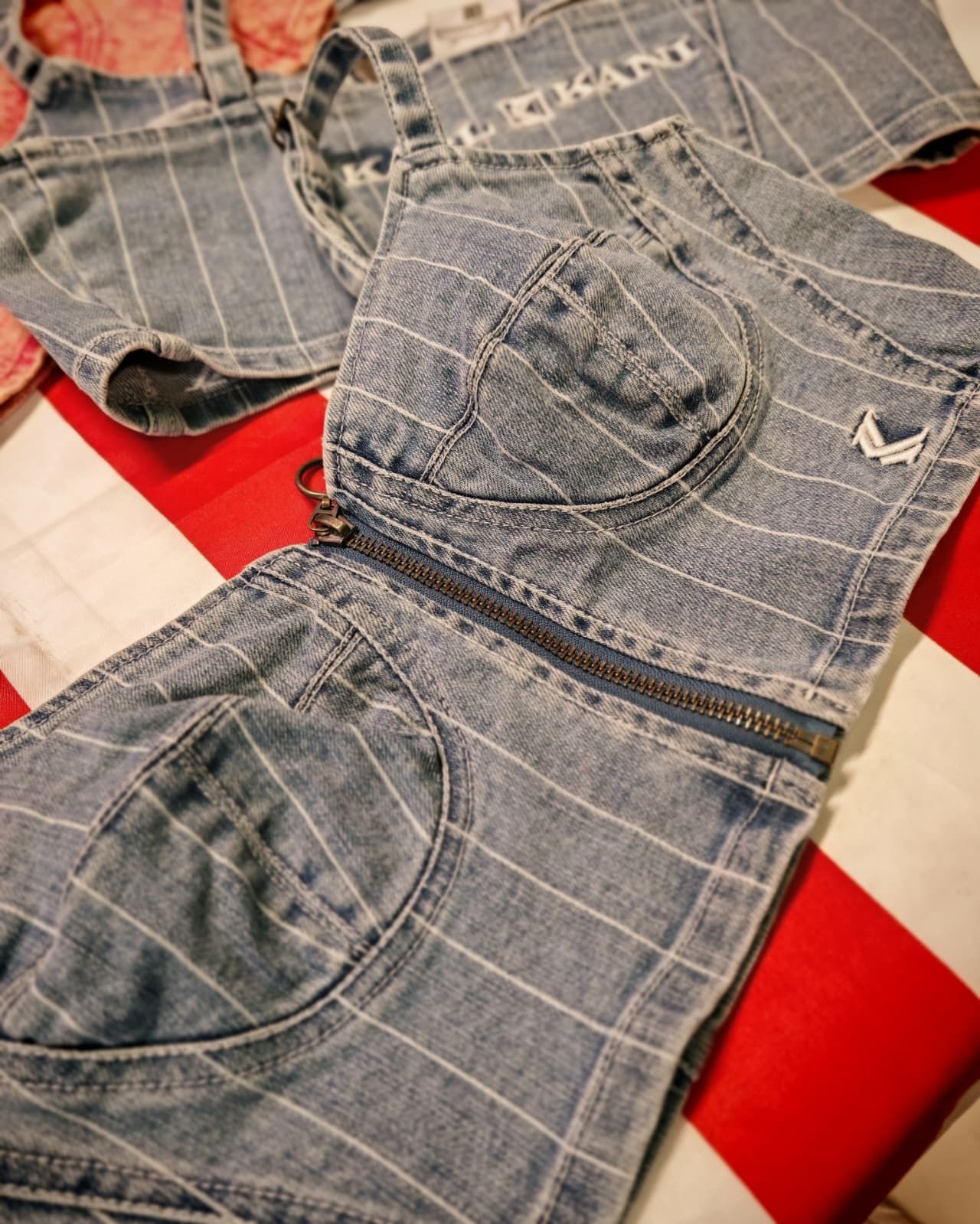 Due corsetti in denim su un tessuto a quadri rossi e bianchi, con cuciture e tasche a vista.