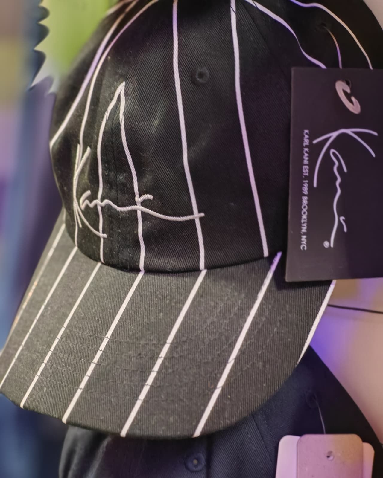 Cappellino da baseball nero a righe sottili con ricamo bianco in stile firma e cartellino pendente.