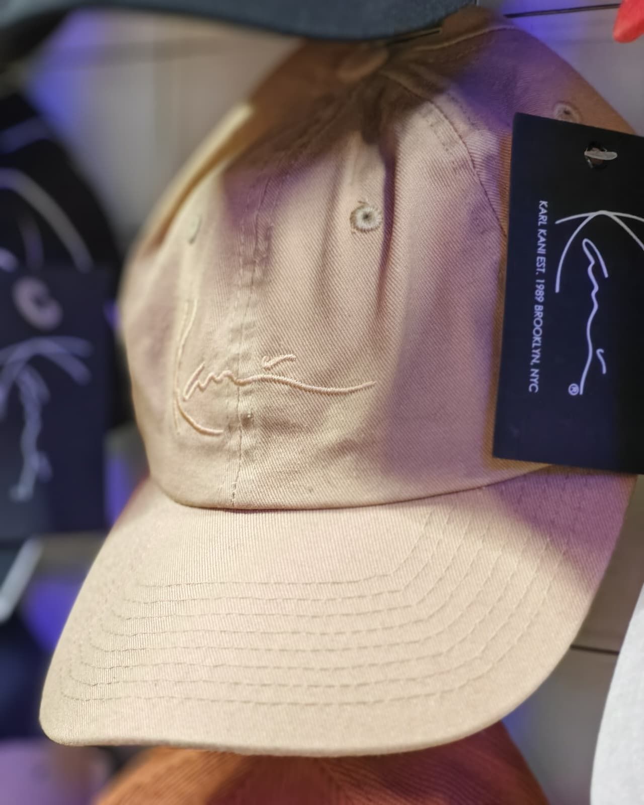 Cappellino da baseball beige con logo ricamato e cartellino appeso, esposto in negozio.