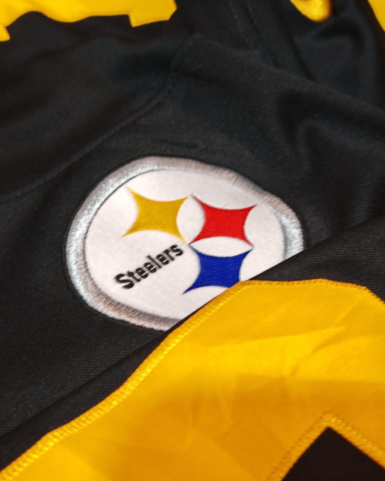 Logo dei Pittsburgh Steelers su tessuto nero e oro.