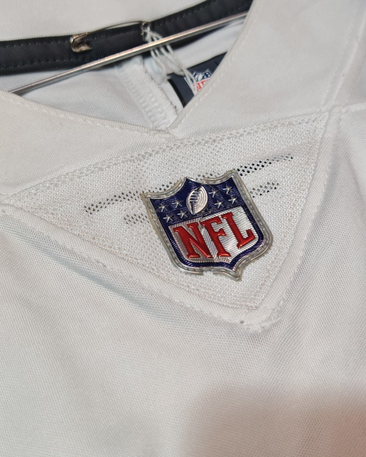 Primo piano del colletto di una maglia bianca della NFL con il logo a scudo della NFL ricamato in rosso, blu e bianco.