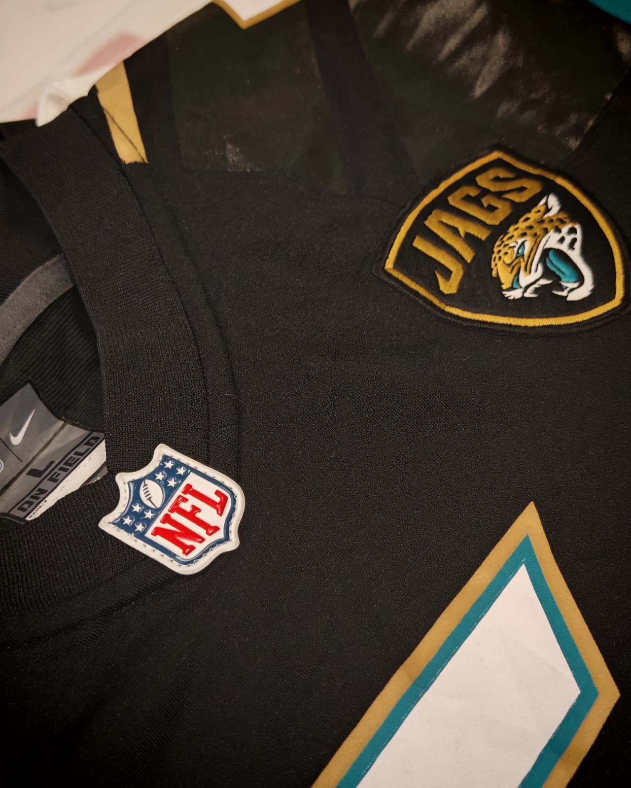 Maglia nera dei Jacksonville Jaguars della NFL con dettagli color verde acqua e oro e numero bianco.