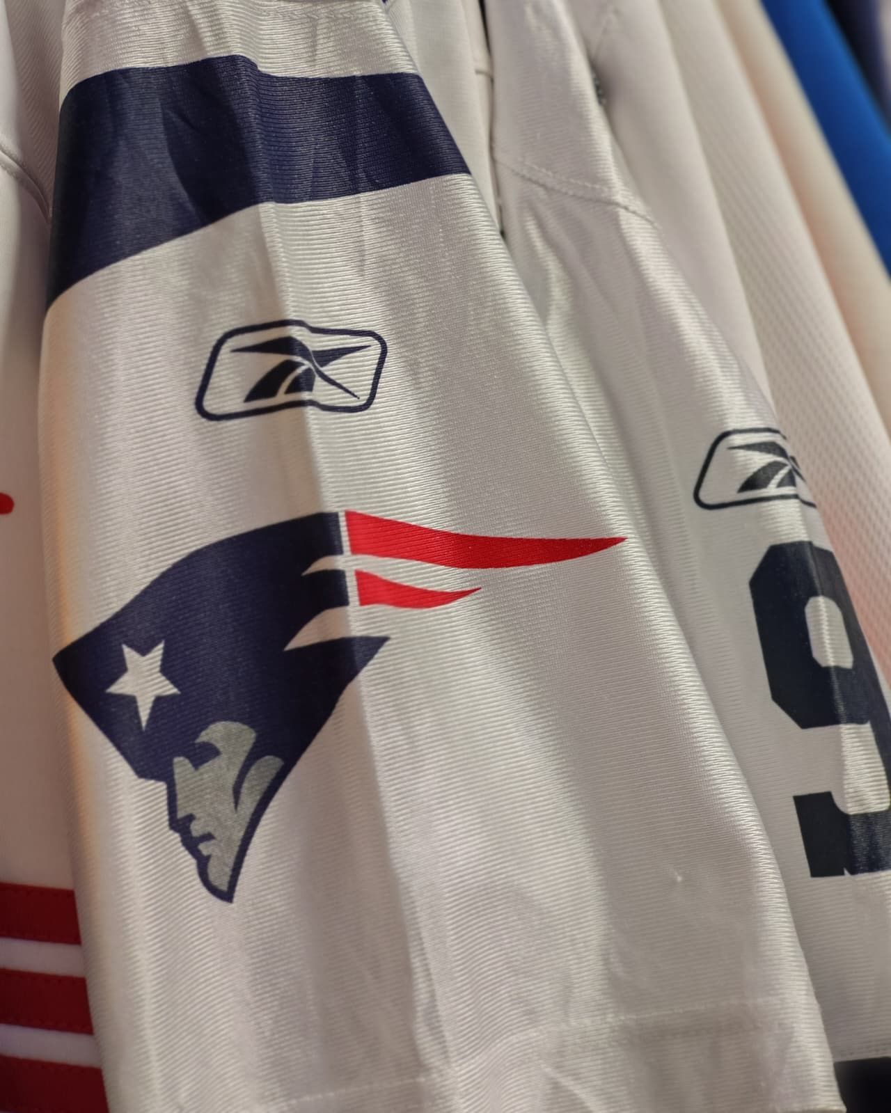 Primo piano di una maglia da football bianca con logo dei Patriots blu navy e rosso e marchio Reebok.