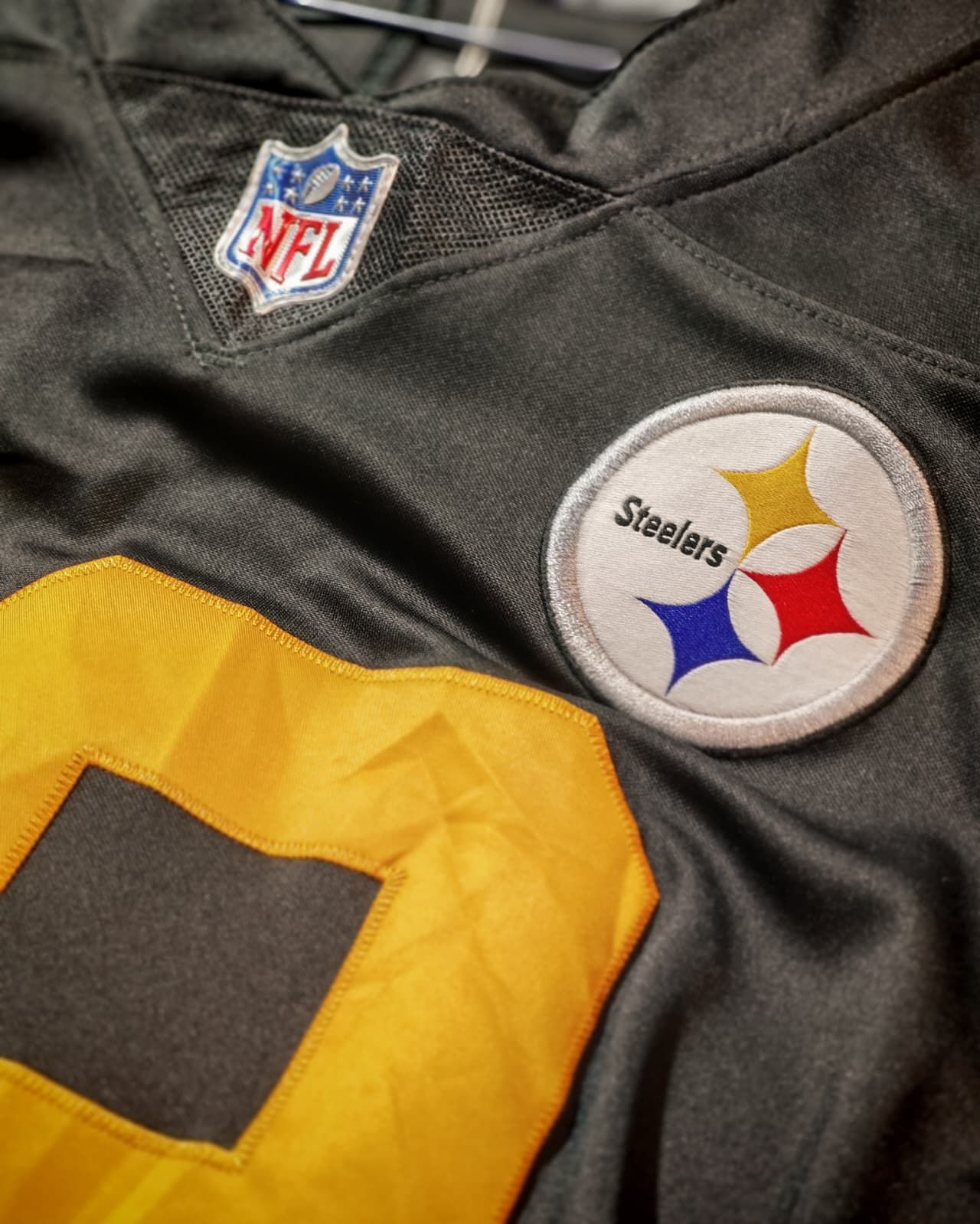 Primo piano di una maglia nera dei Pittsburgh Steelers con le patch della NFL e del logo della squadra sul petto.