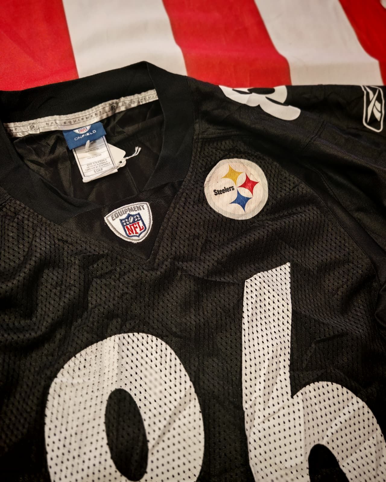 Maglia nera dei Pittsburgh Steelers con grandi numeri bianchi e logo della squadra su sfondo rosso e bianco.