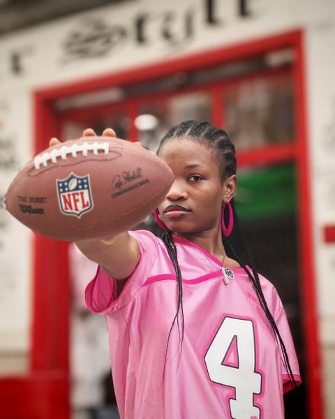 Persona con maglia rosa che tiene in mano un pallone da football americano della NFL, rivolto verso la telecamera.