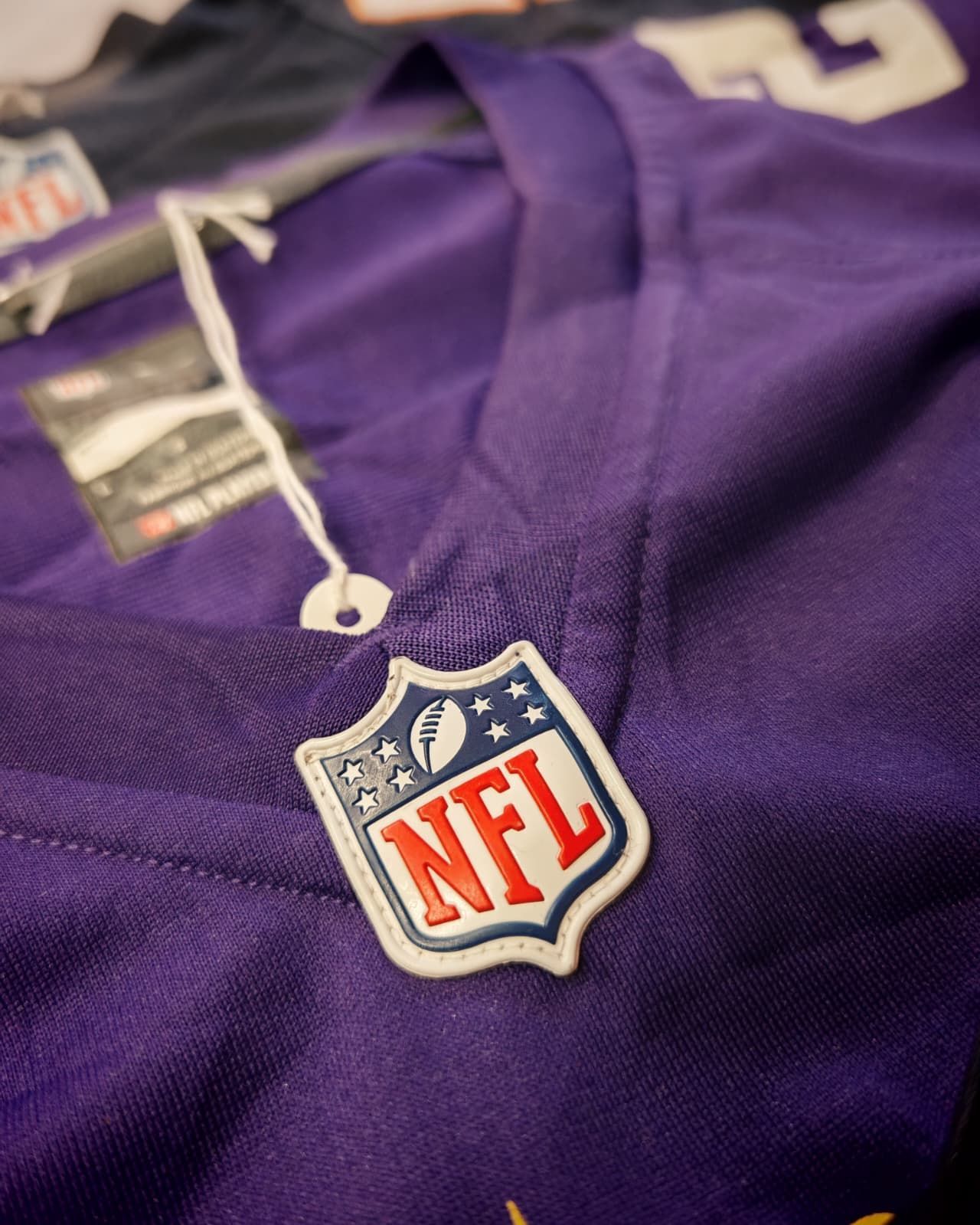 Primo piano di una maglia viola della NFL con il logo a scudo della lega e cuciture bianche.