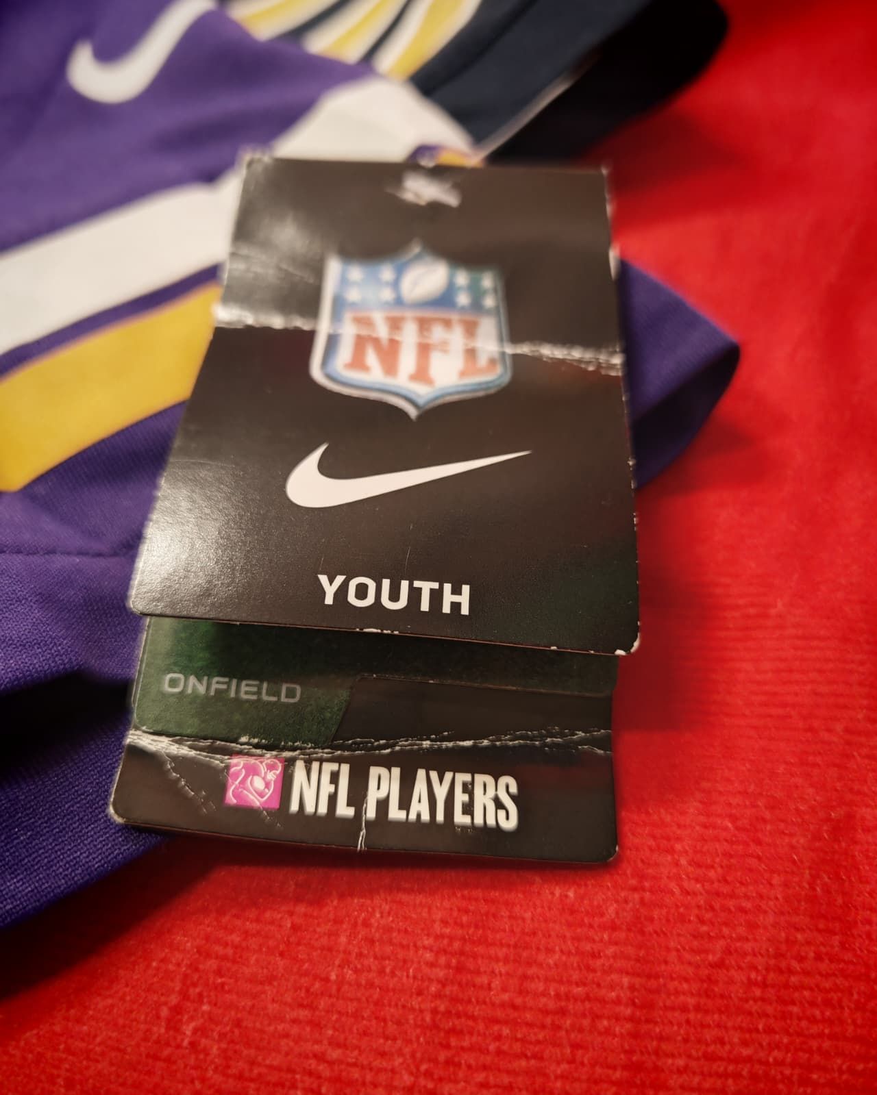 Etichetta da maglia giovanile NFL su tessuto viola e rosso, con i loghi Nike e NFL Players.