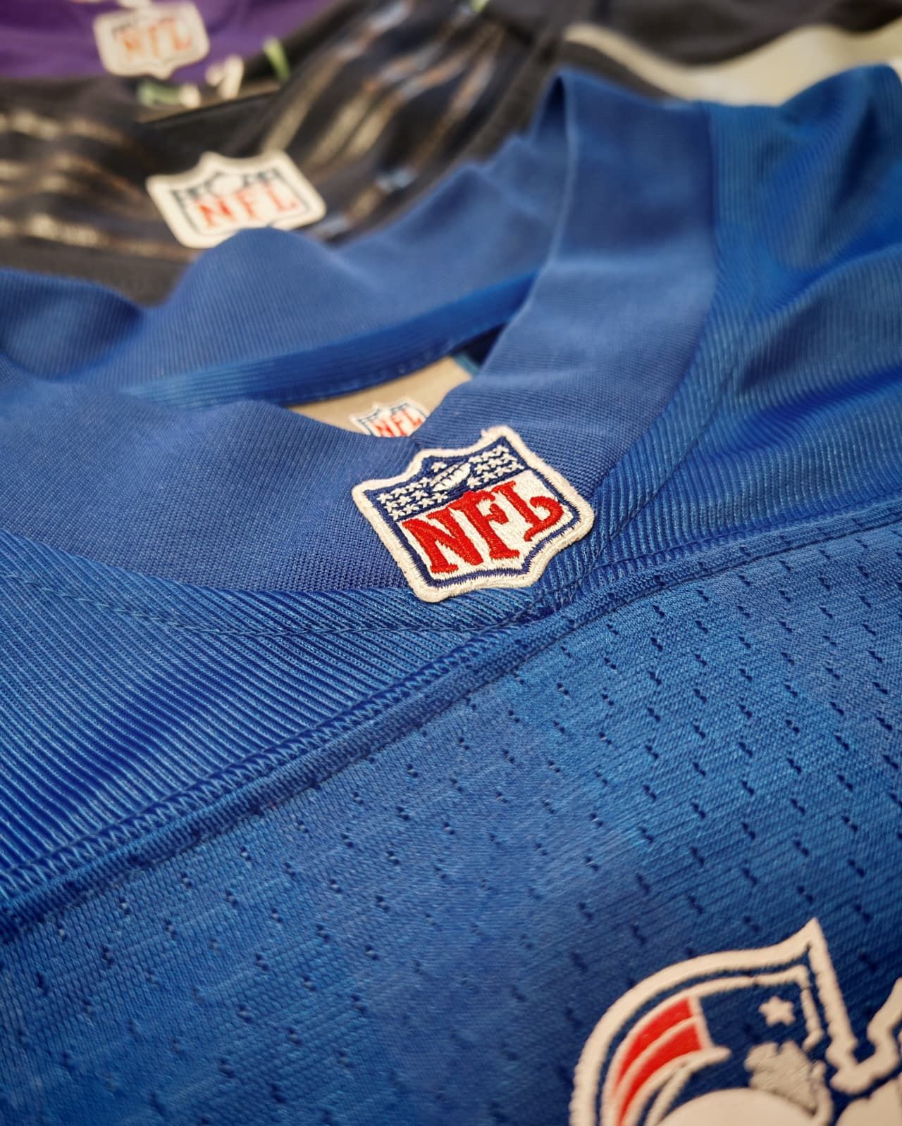 Primo piano di maglie da football americano NFL blu e nere con loghi ricamati e tessuto a rete.
