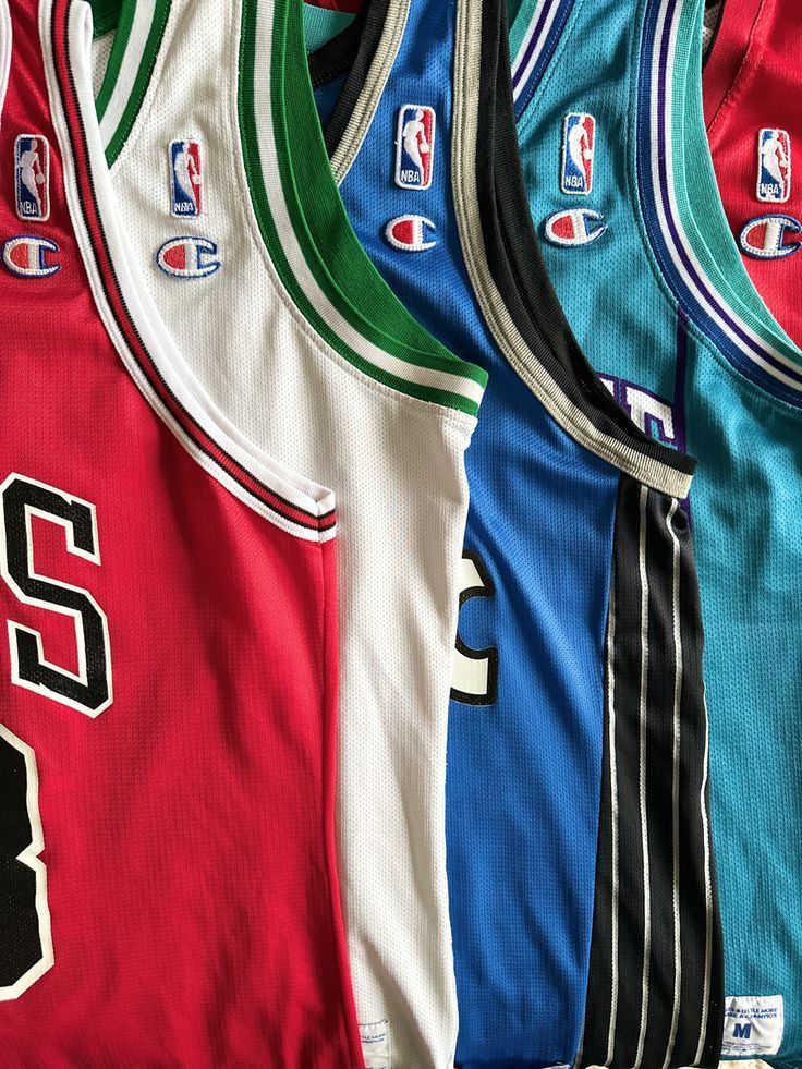 Diverse maglie da basket NBA nei colori rosso, verde, nero, blu e turchese, appese una accanto all'altra.