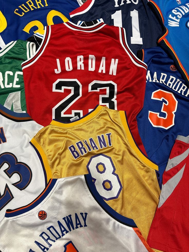 Maglie da basket disposte in fila, tra cui la numero 23 di Jordan, la numero 8 di Bryant e la numero 3 di Marbury, nei colori rosso, oro e blu.