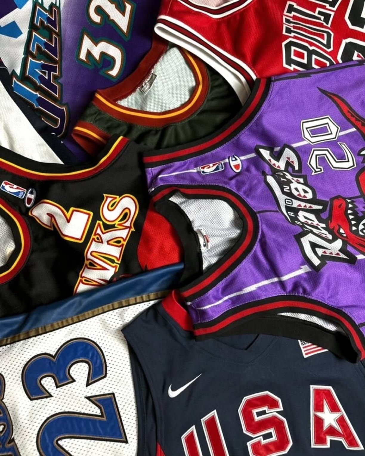 Maglie da basket sovrapposte nei colori viola, nero, rosso e bianco, con loghi e numeri delle squadre.