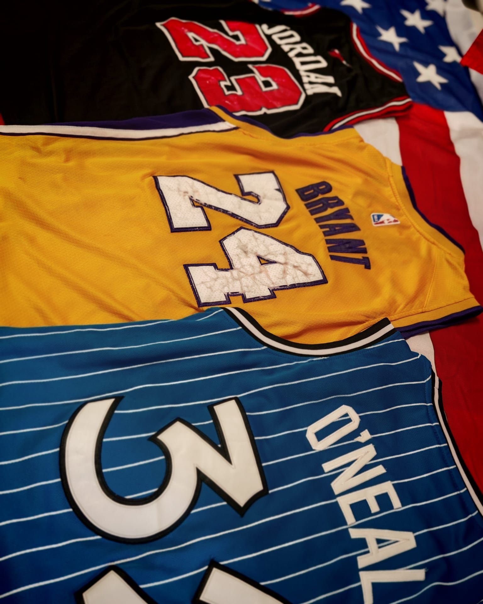 Tre maglie sportive disposte in fila: la numero 29 nera, la numero 24 gialla di Bryant e la numero 3 a righe blu di O'Neal.