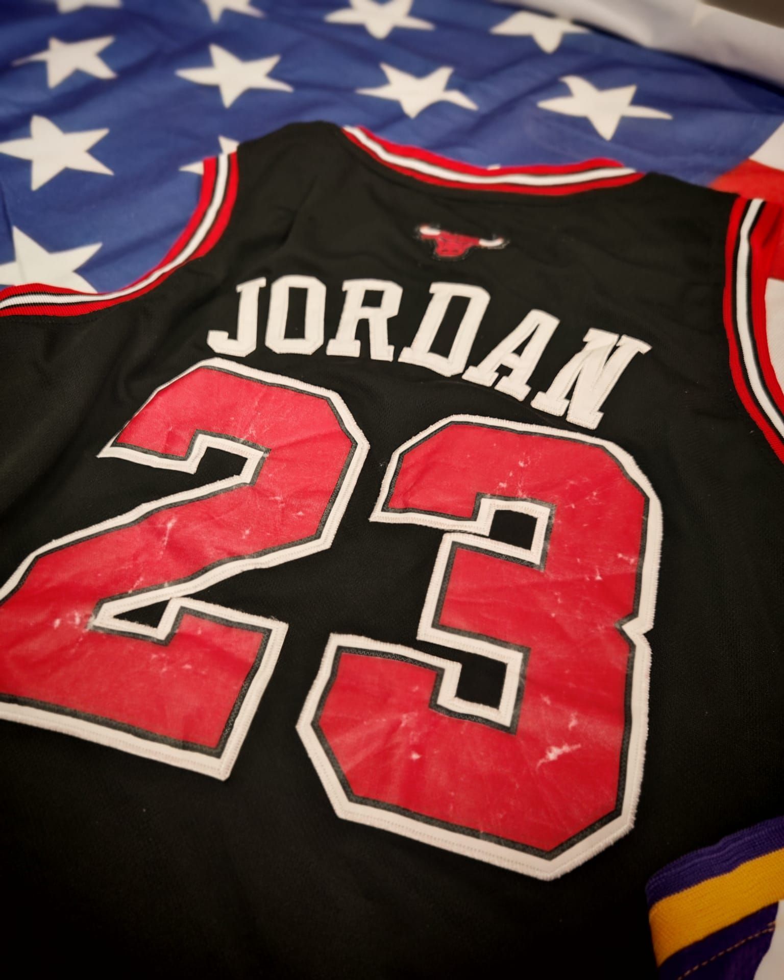Maglia nera dei Chicago Bulls Jordan 23 con finiture rosse e bianche su una coperta blu con motivo a stelle.