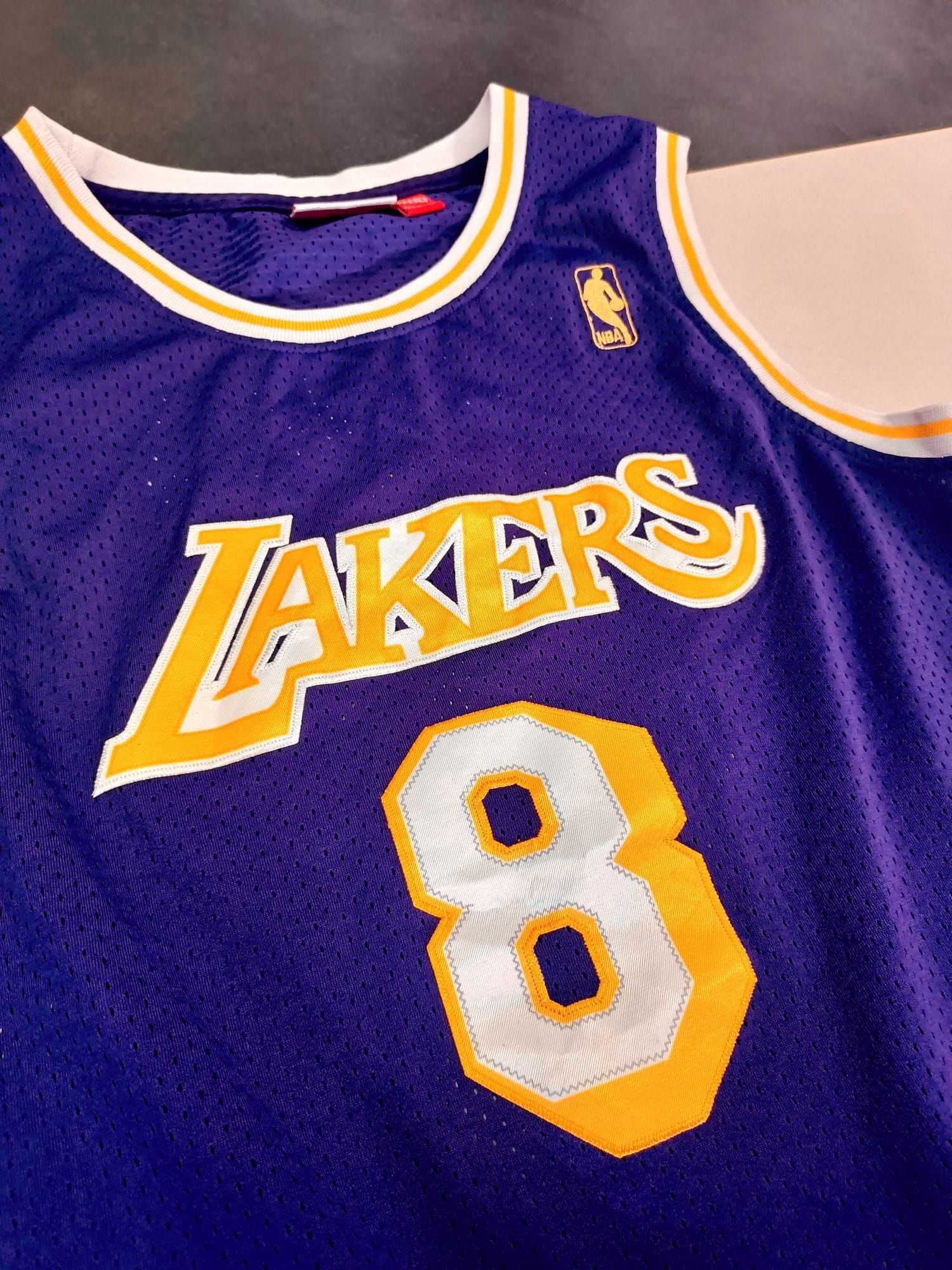 Maglia viola dei Los Angeles Lakers con il numero 8 e finiture dorate, stesa su una superficie