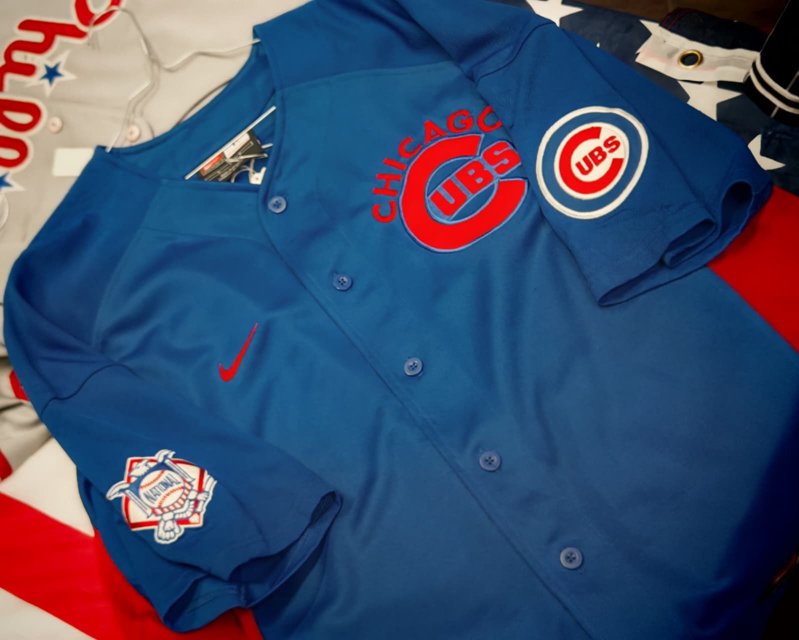 Maglia blu dei Chicago Cubs con dettagli rossi e logo della squadra, adagiata su un letto.