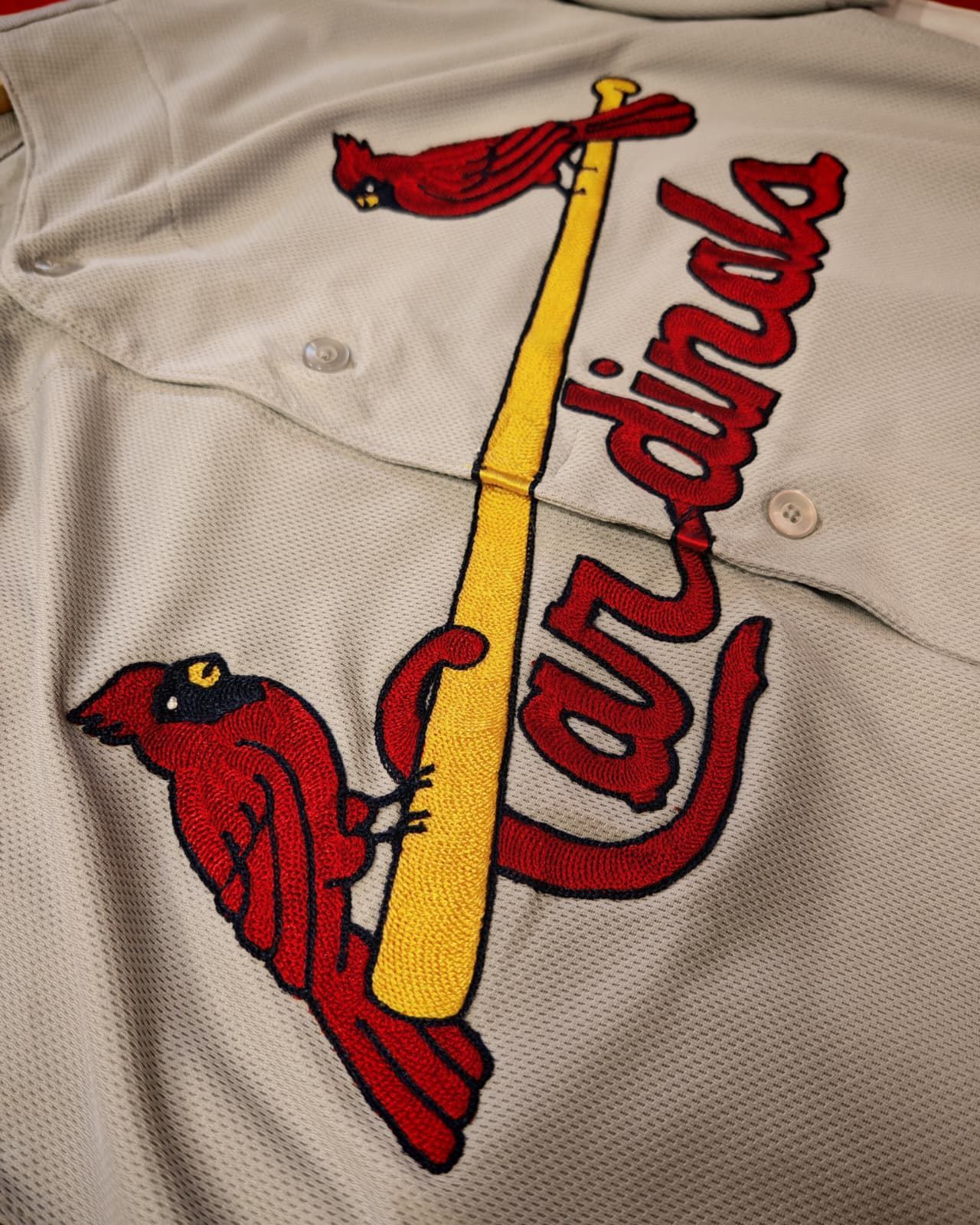 Logo rosso dei St. Louis Cardinals con due cardinali appollaiati su una mazza gialla su una maglia bianca.