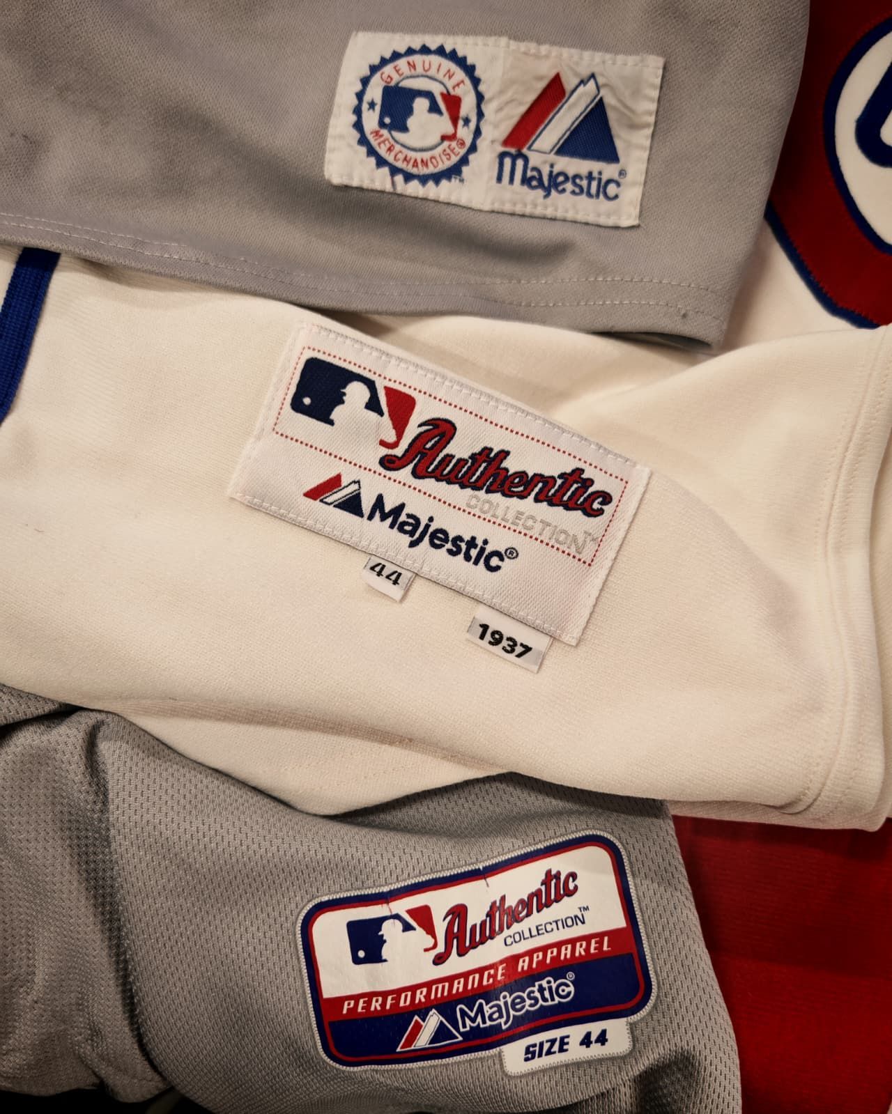 Etichette sovrapposte per abbigliamento da baseball, nei colori grigio, crema e rosso, con i loghi Majestic e MLB.