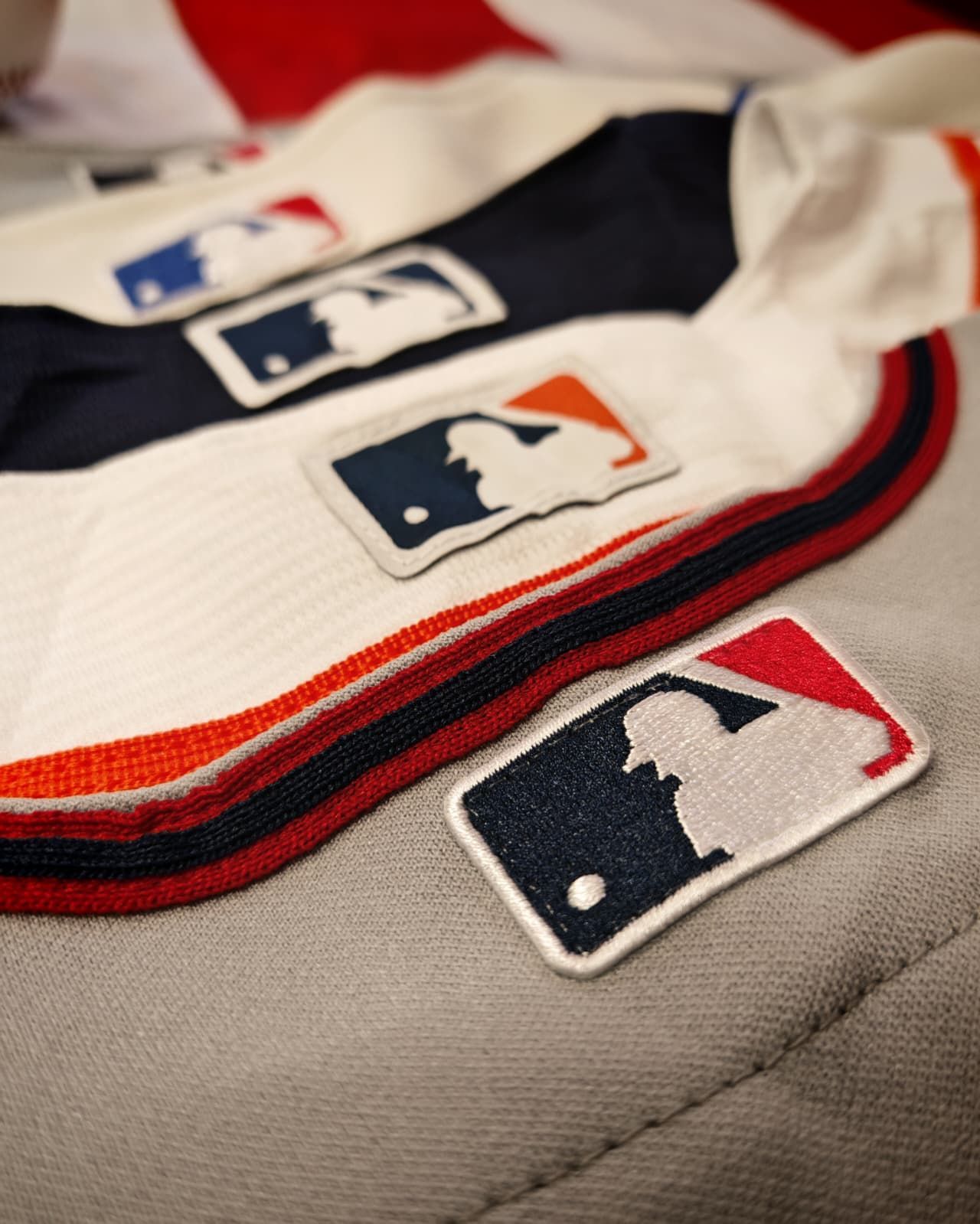 Primo piano di maglie da baseball con patch con il logo della MLB nei colori bianco, blu scuro e rosso.