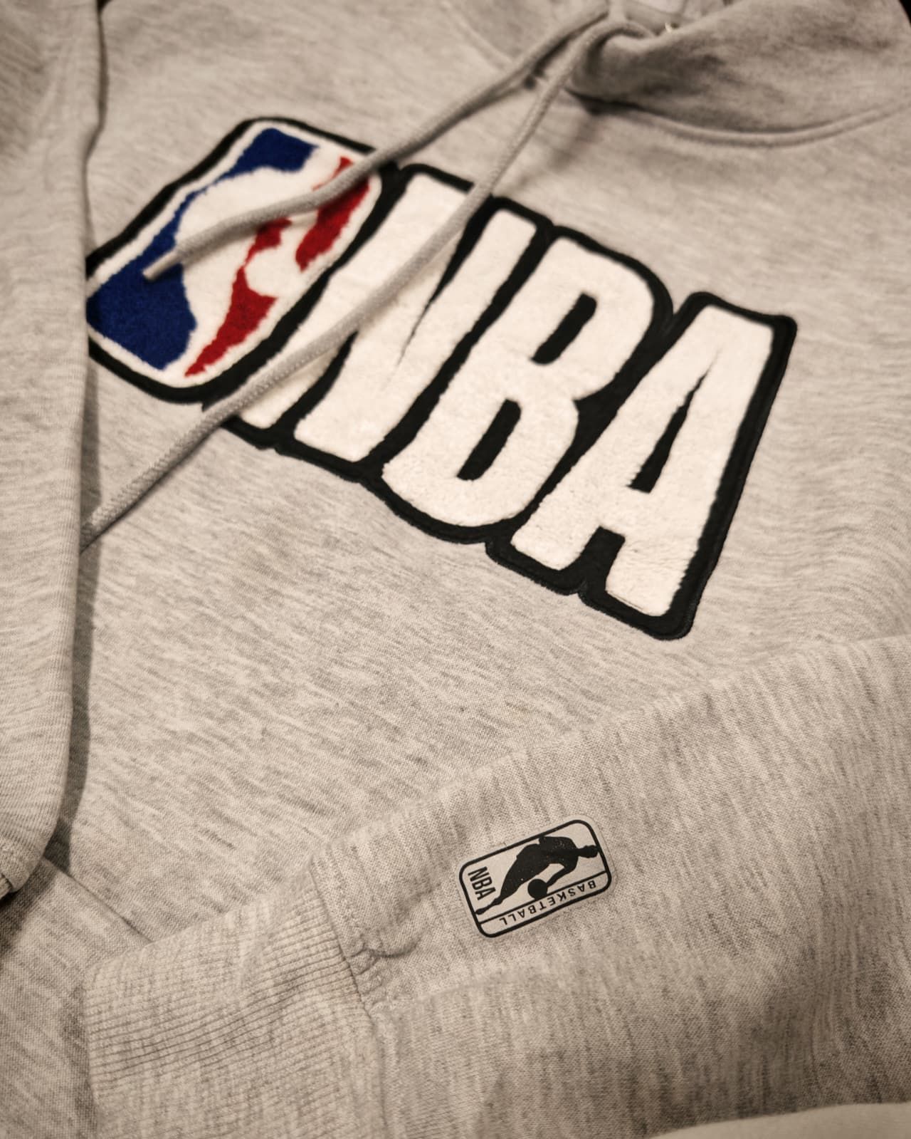 Felpa grigia con cappuccio, grande logo NBA e piccola etichetta NBA.