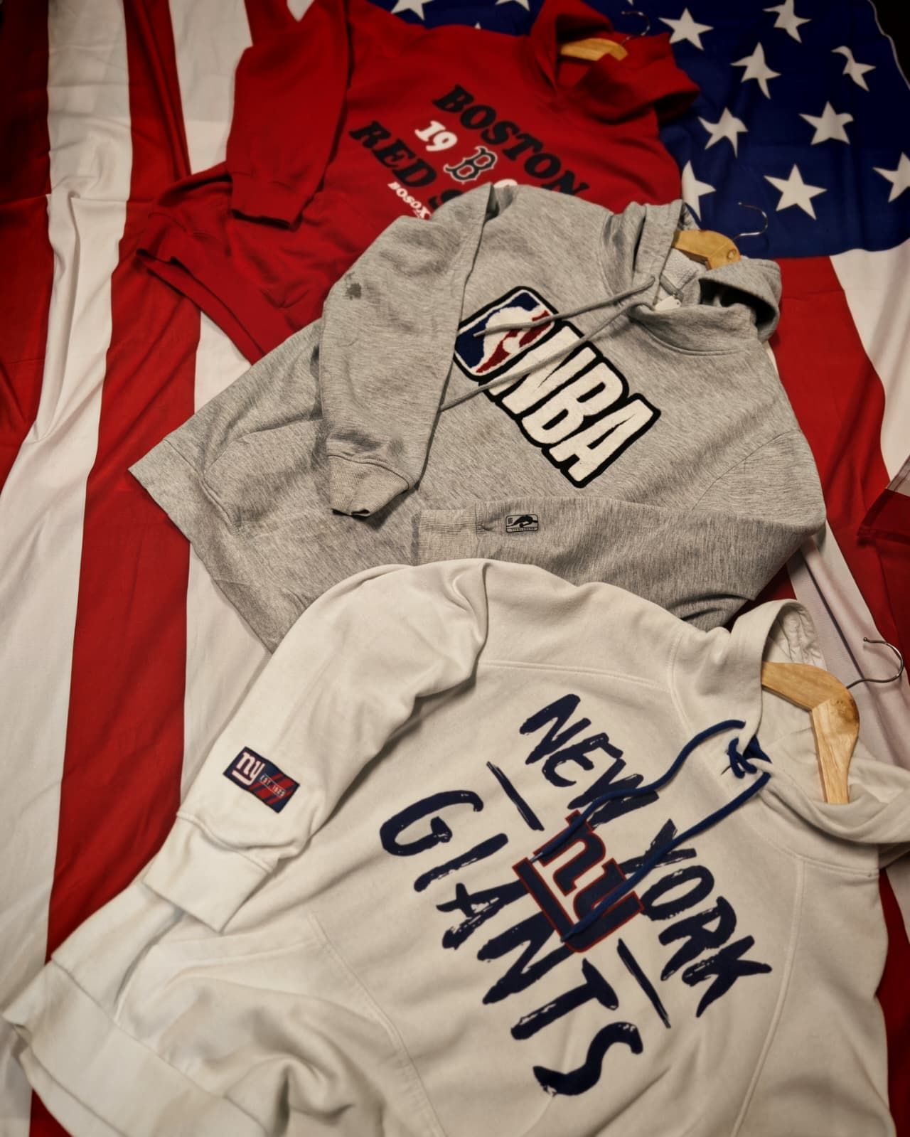 Quattro felpe sportive piegate, nei colori rosso, grigio e bianco, su uno sfondo con la bandiera americana.