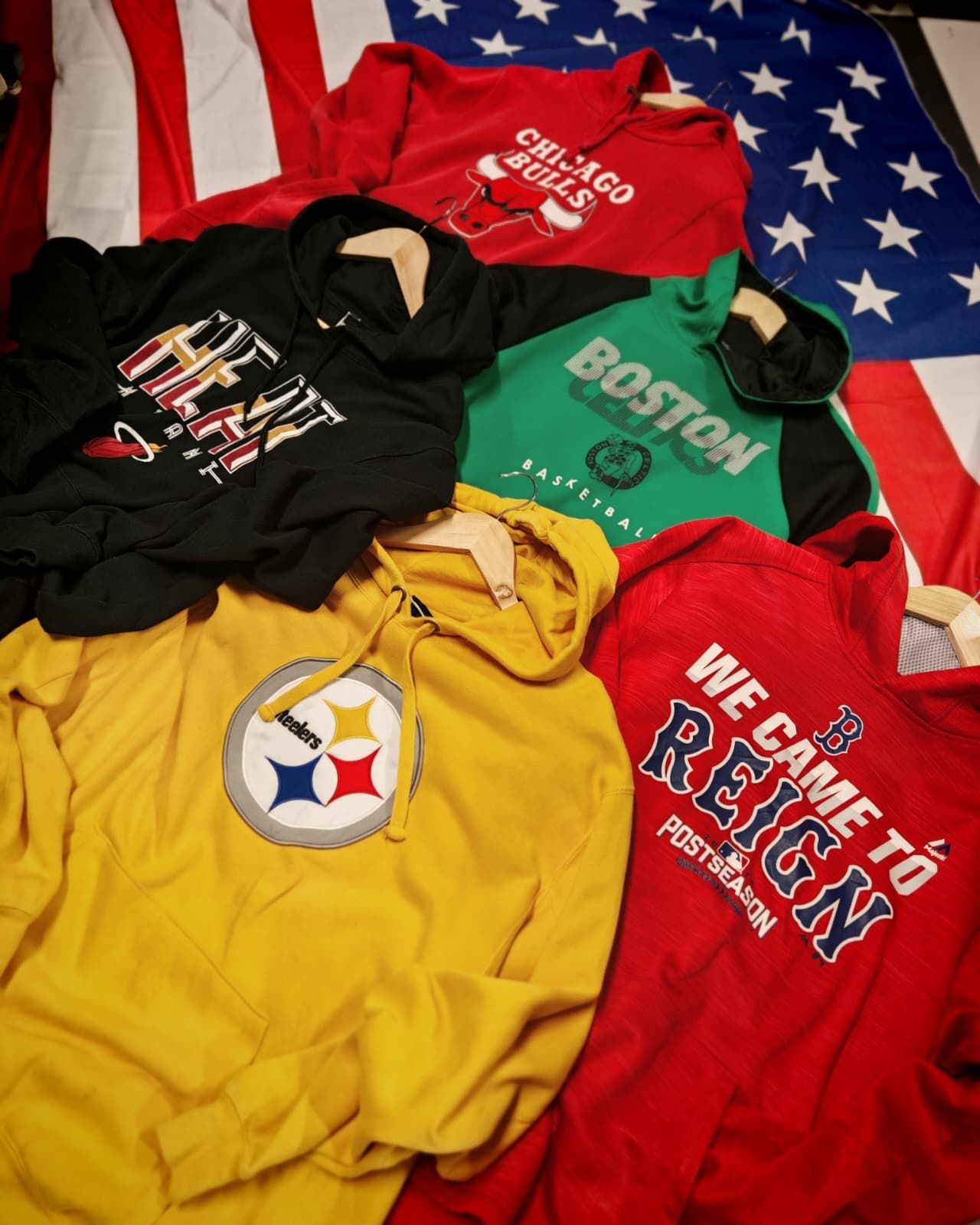 Quattro felpe con cappuccio colorate su uno sfondo con la bandiera americana, decorate con slogan sportivi e cittadini.