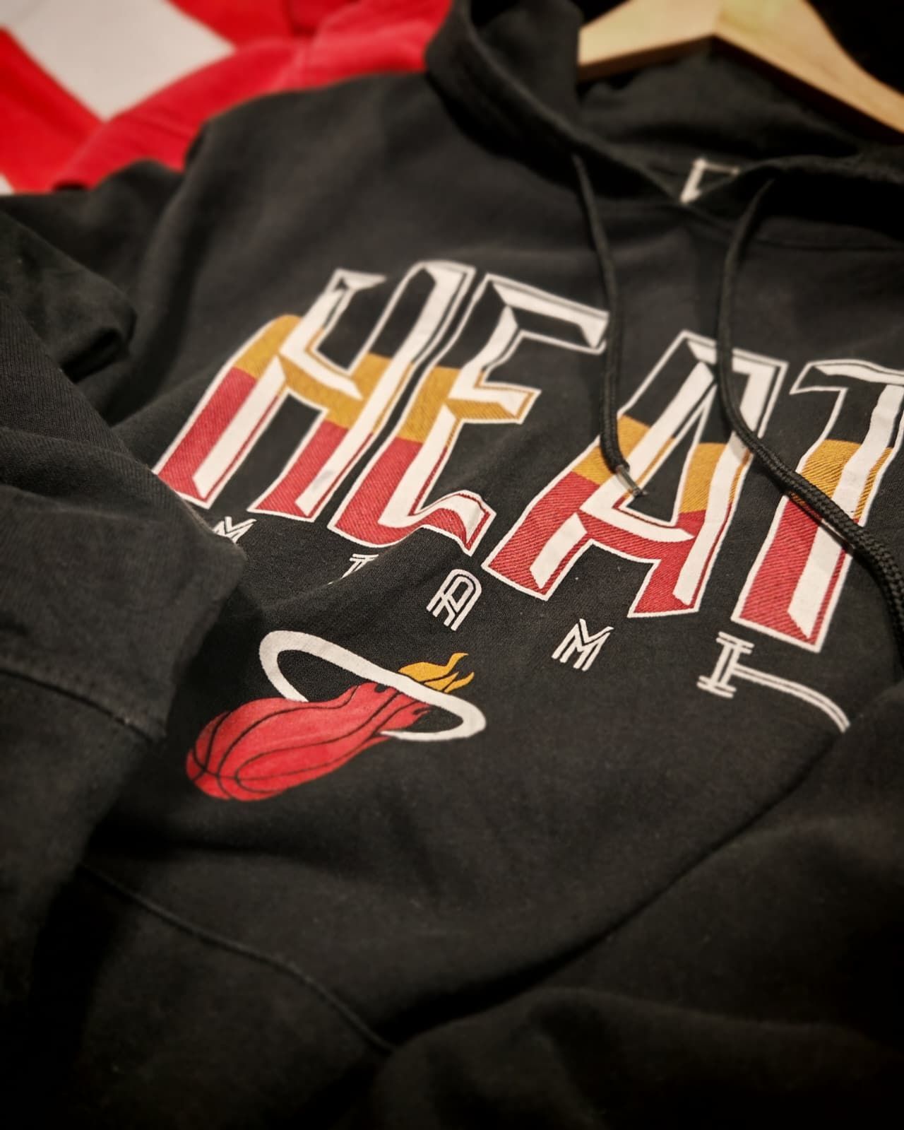 Felpa nera con cappuccio dei Miami Heat con logo e grafica di un pallone da basket rosso appesa a una gruccia.