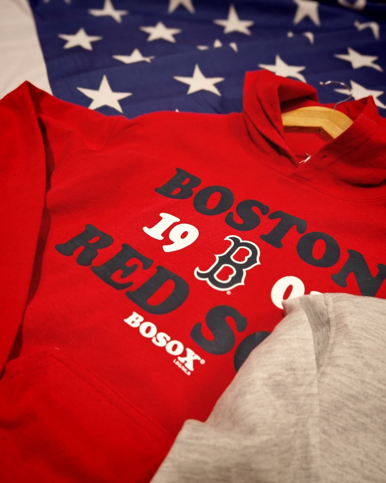 Felpa rossa dei Boston Red Sox su sfondo con la bandiera americana, con un panno grigio nell'angolo.