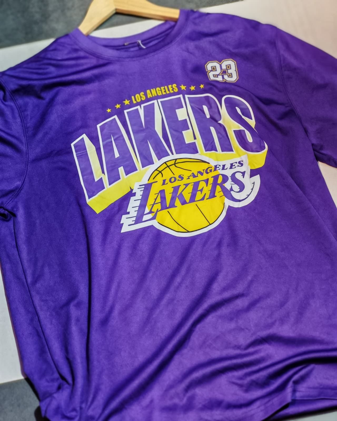 Maglietta viola dei Los Angeles Lakers con grandi loghi della squadra dorati e bianchi appesa a una gruccia.