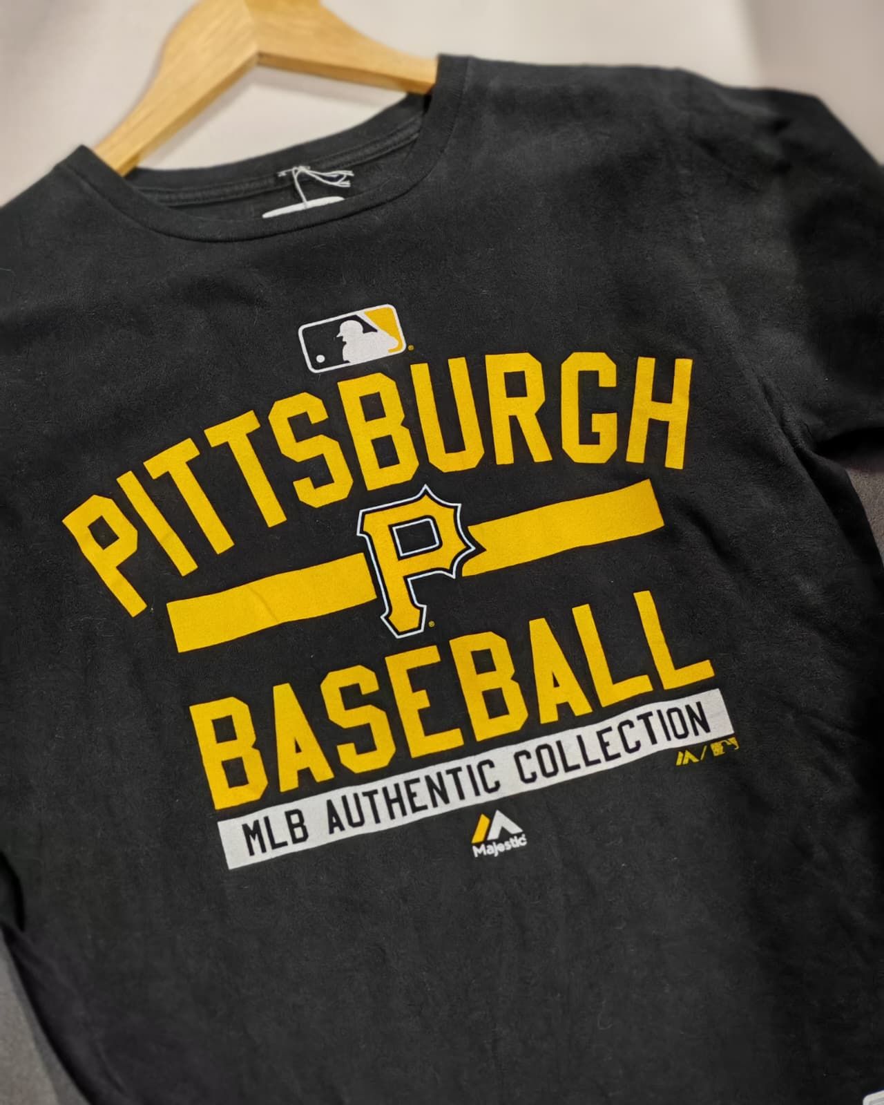 Maglietta nera da baseball dei Pittsburgh Pirates appesa a una gruccia, con scritta gialla e logo MLB Authentic Collection.