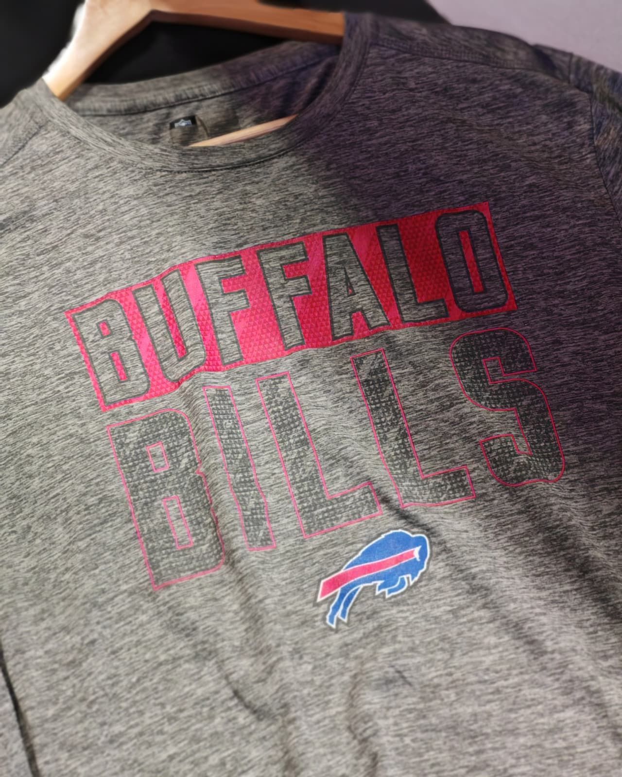 Maglietta grigia dei Buffalo Bills con scritta rossa e logo della squadra appesa a una gruccia.