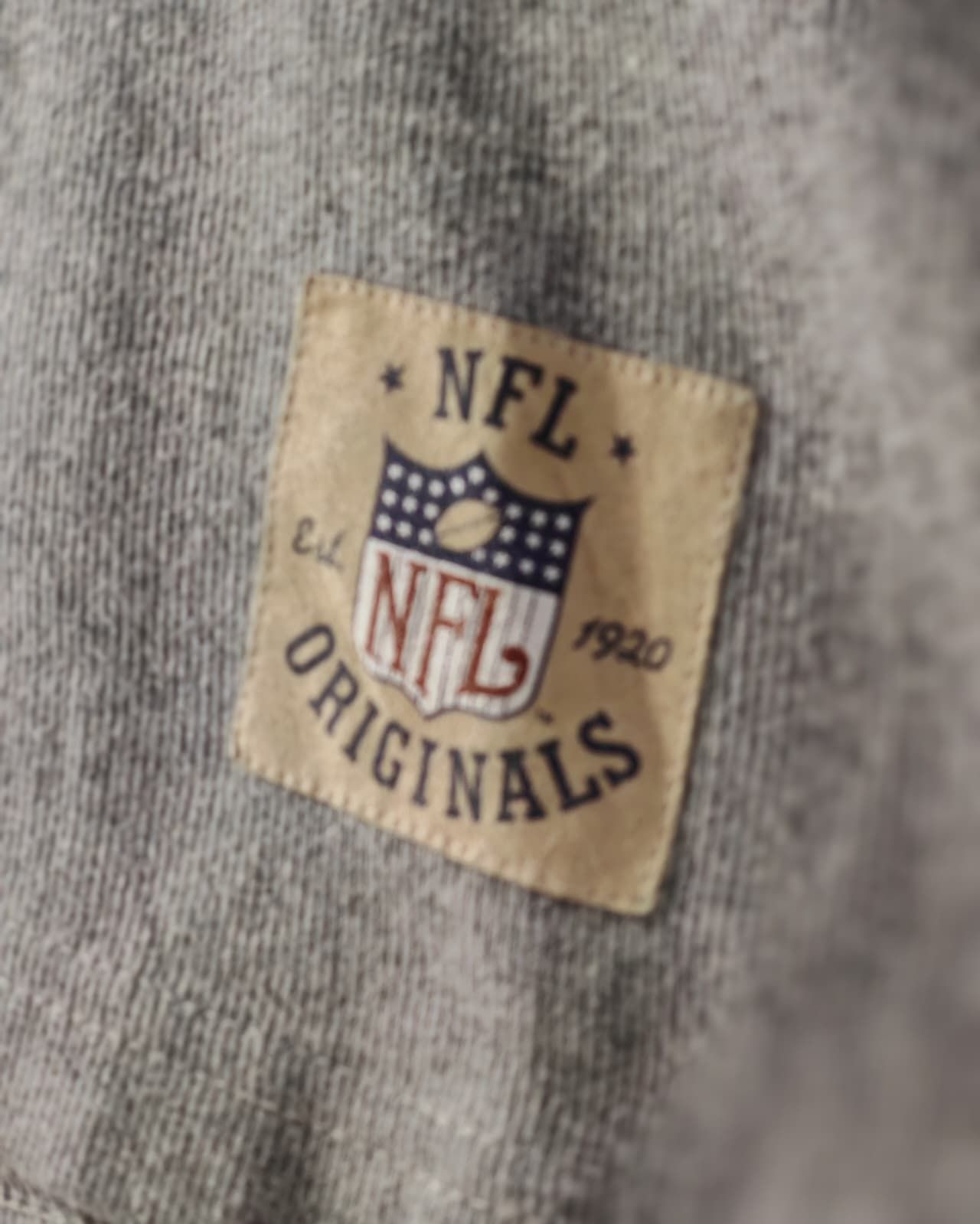 Primo piano di una maglietta grigia con una toppa color beige con il logo NFL Originals.