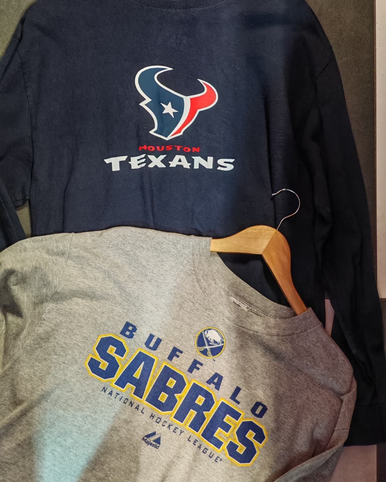 Due magliette sportive appese: una blu navy degli Houston Texans e una grigia dei Buffalo Sabres.