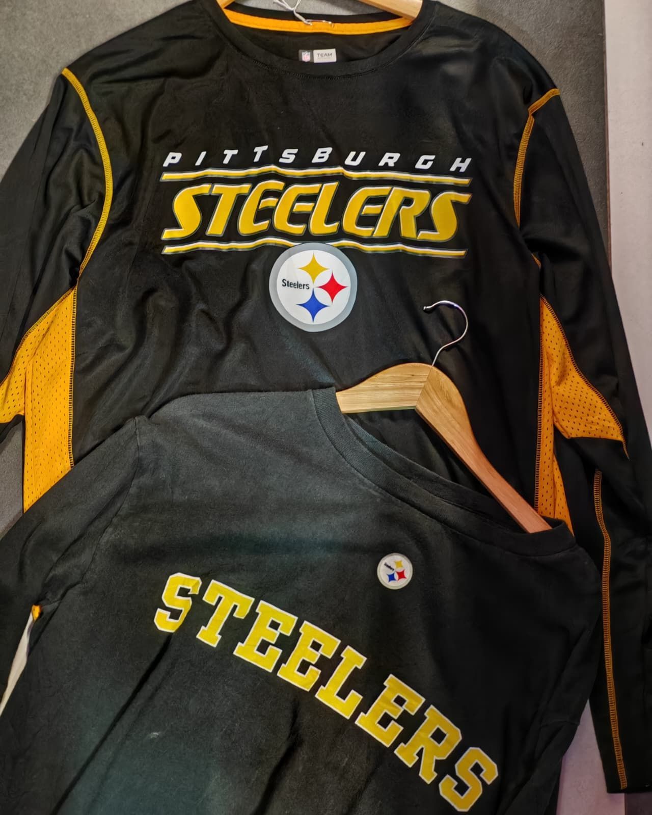 Maglia nera dei Pittsburgh Steelers e camicia abbinata con dettagli dorati, disposte su un letto.