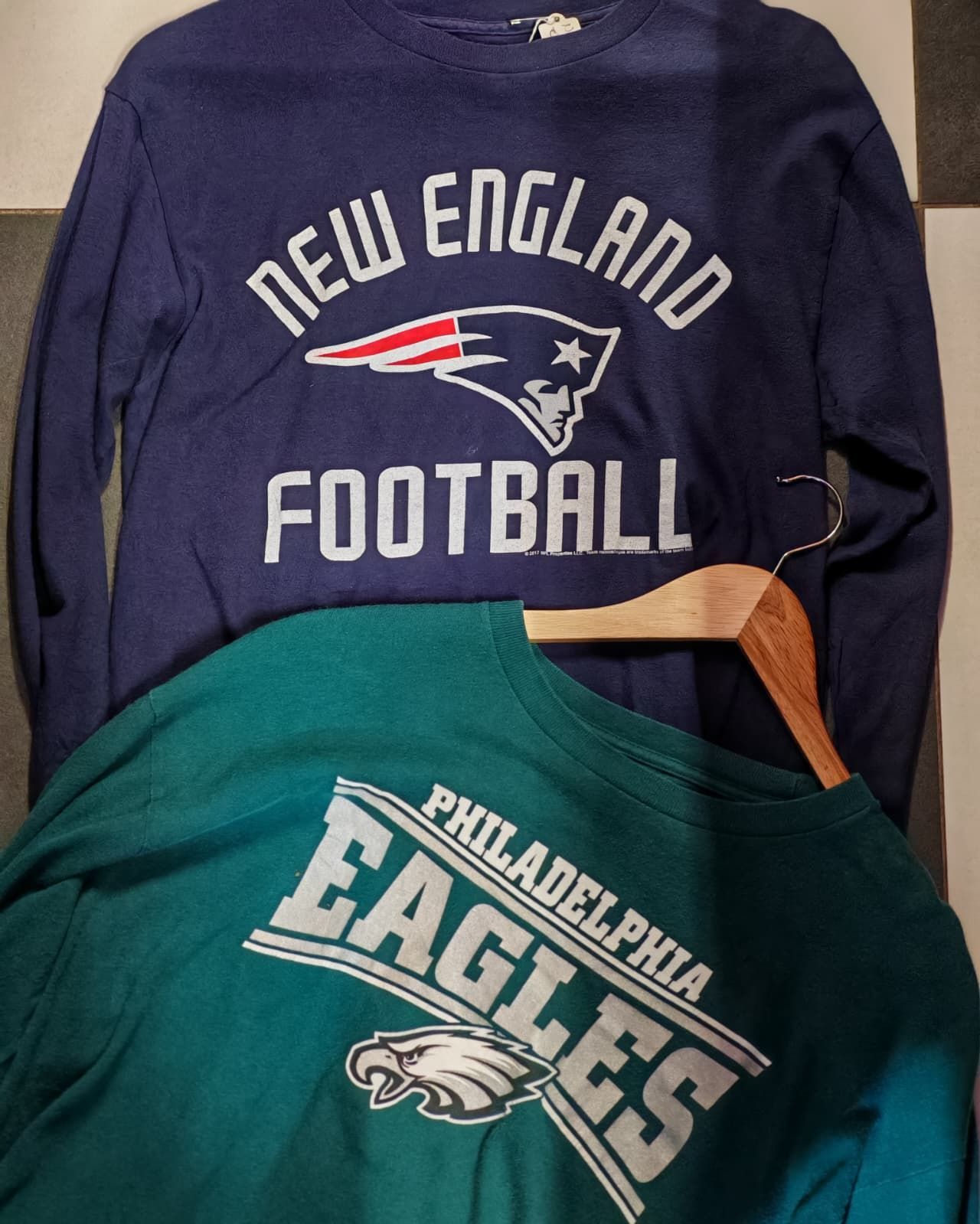 Due magliette della NFL sovrapposte: quella blu scuro dei New England Patriots sopra, quella verde dei Philadelphia Eagles sotto.