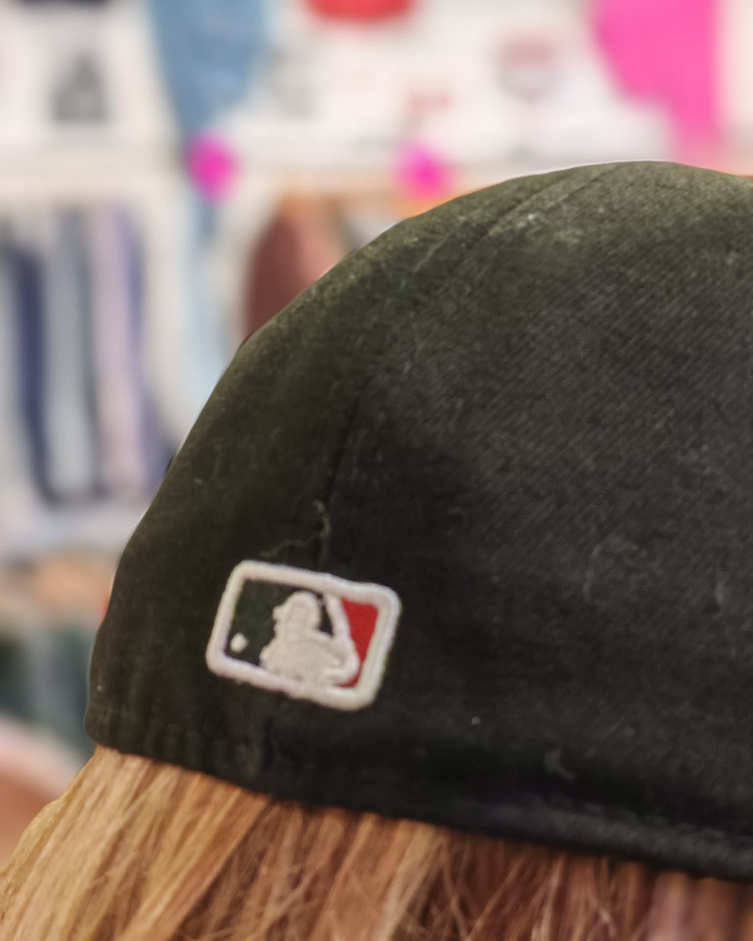 Primo piano di un berretto da baseball nero con il logo MLB su uno sfondo sfocato di un negozio di abbigliamento.