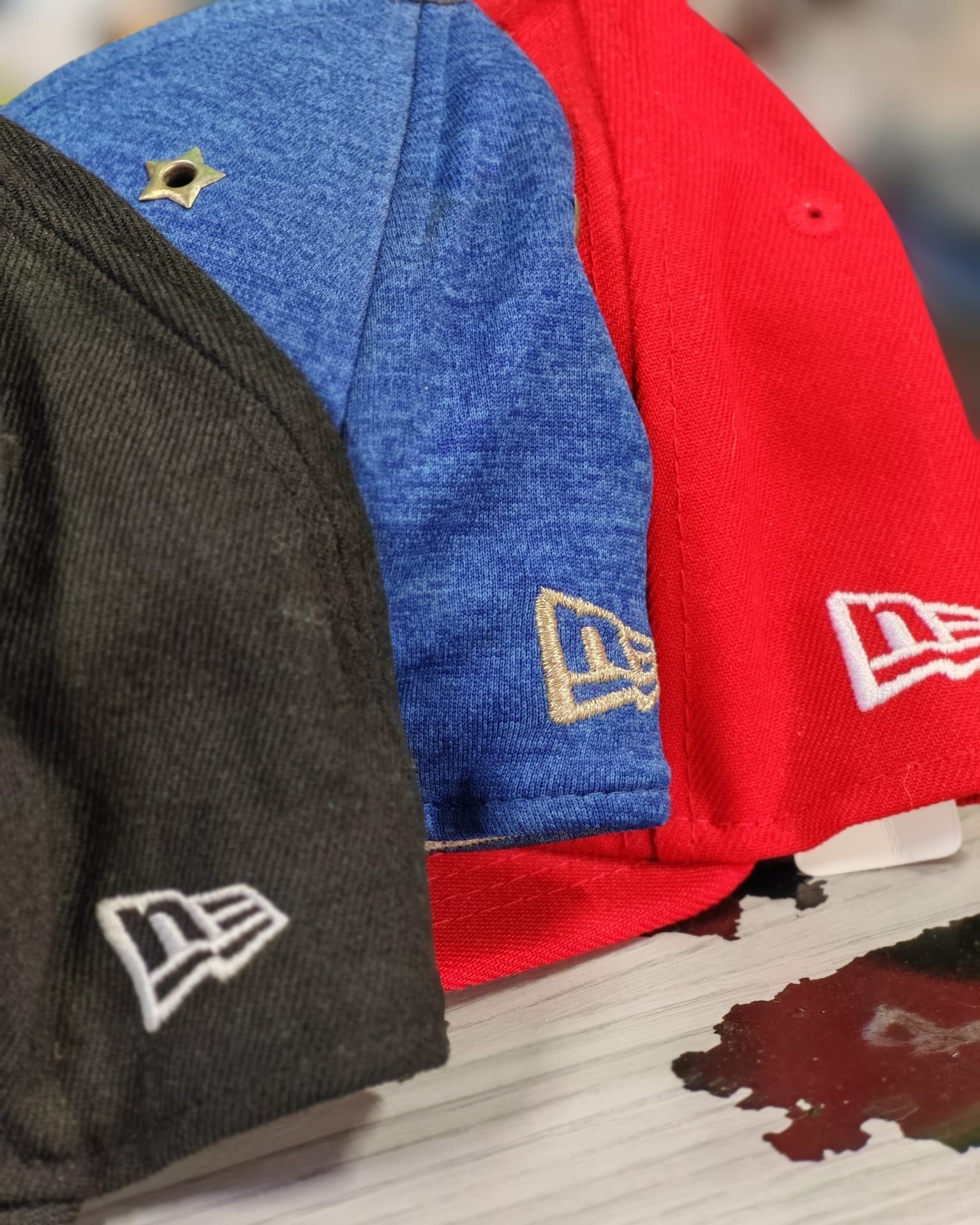 Tre cappellini da baseball New Era, uno nero, uno blu e uno rosso, impilati su un tavolo.