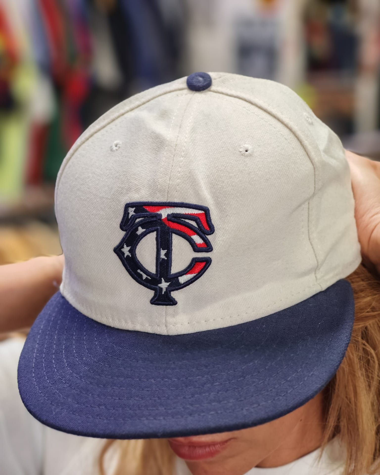 Berretto da baseball bianco e blu scuro con logo TC rosso e blu, indossato da una persona all'aperto.