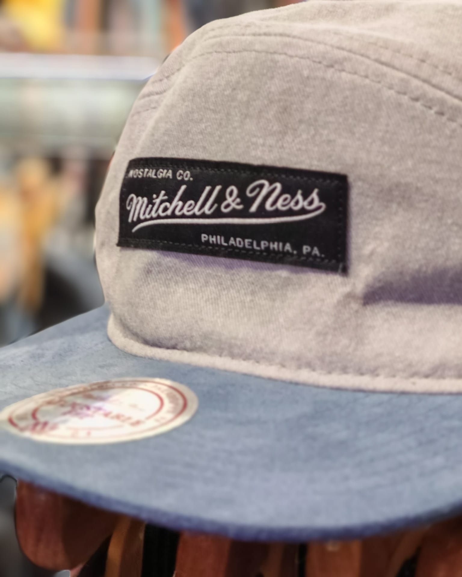 Primo piano di un berretto Mitchell & Ness beige e blu con una toppa con il logo nera.