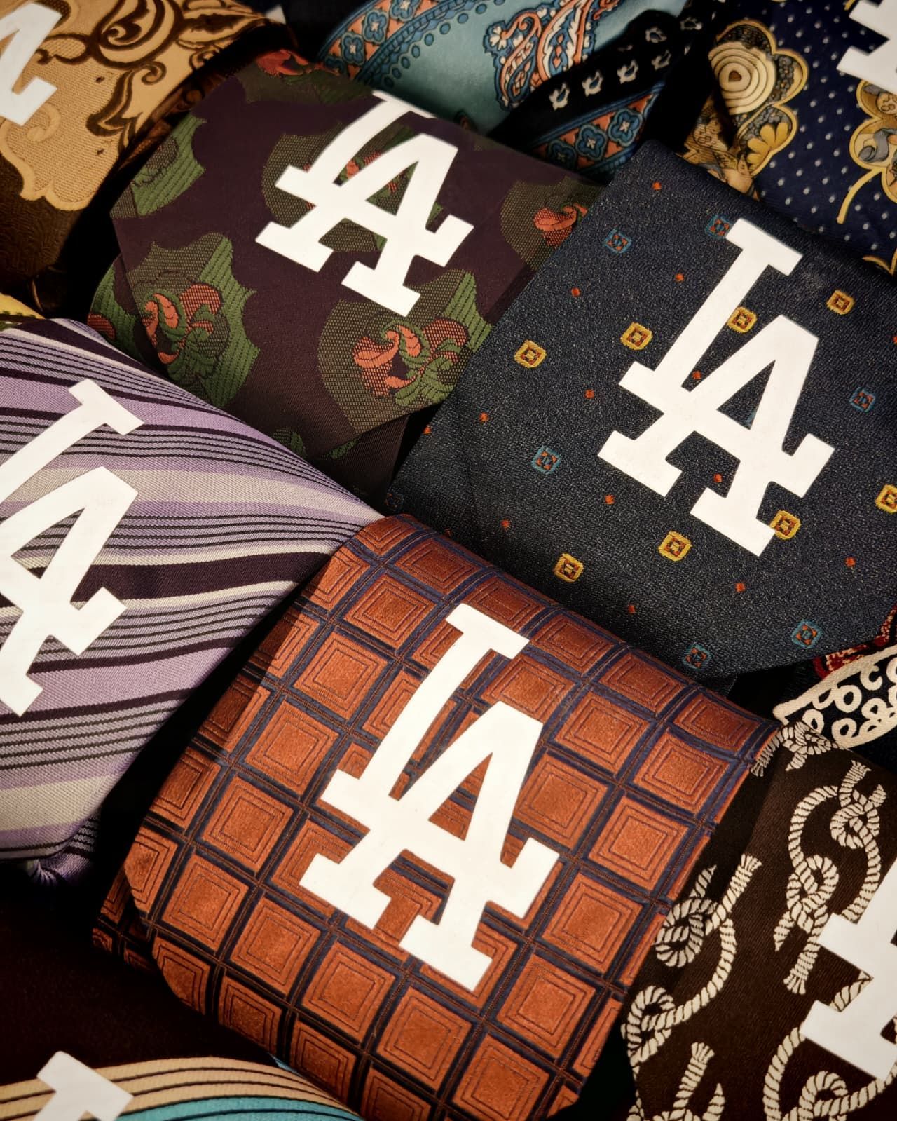 Cravatte assortite con il logo LA, in diversi colori e fantasie, impilate una accanto all'altra.