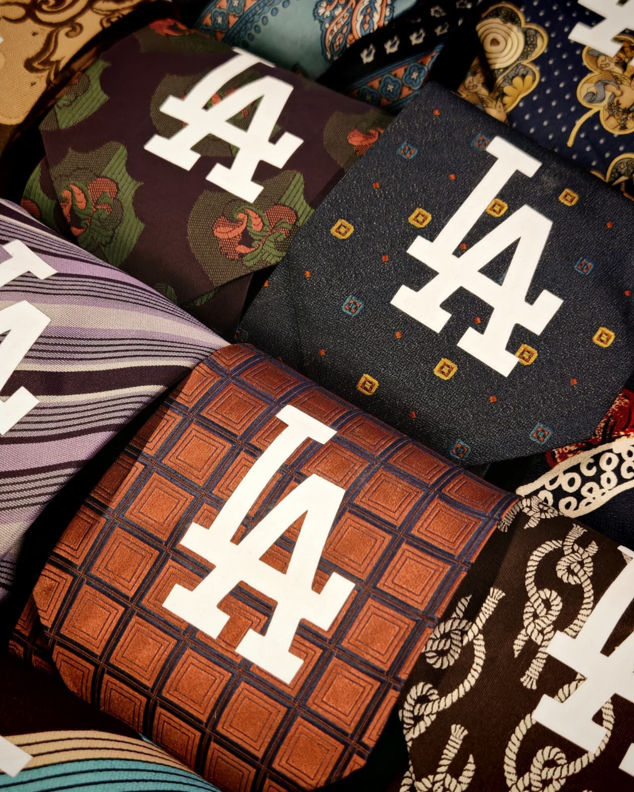 Assortimento di pochette in tessuto con logo LA, disponibili nei colori nero, marrone e viola con scritte bianche.