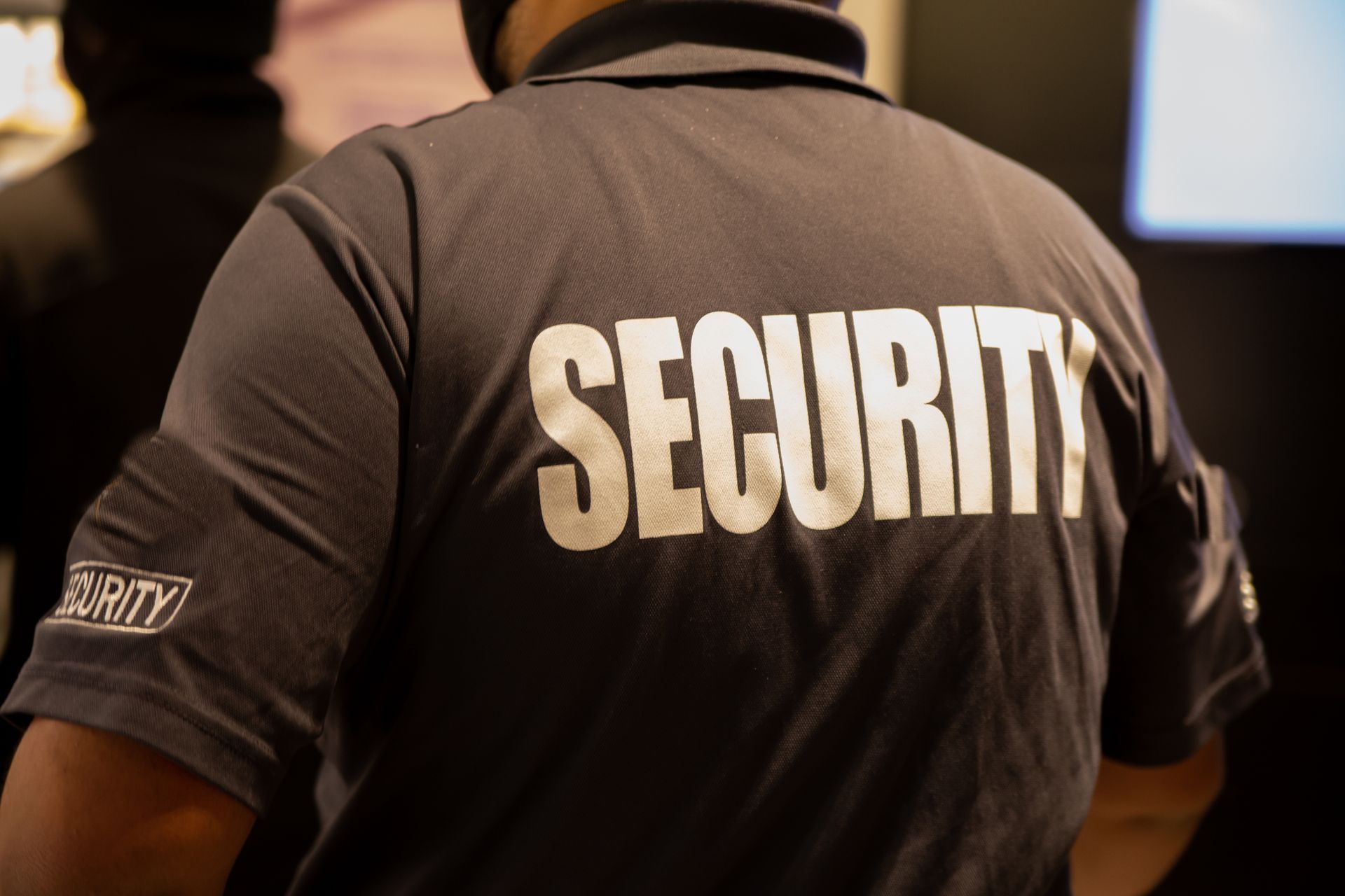 Close-up of security guard wearing black shirt with bold “SECURITY” text on back. Close-up of security guard wearing black shirt with bold “SECURITY” text on back.
