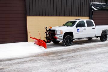 White pickup truck with a red snowplow clearing snow in front of a building.