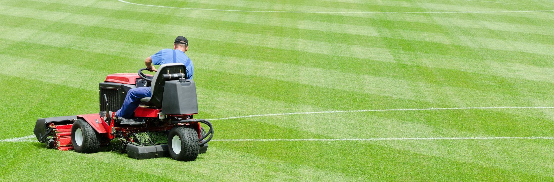 Person riding a red lawn mower on a green striped grass field
